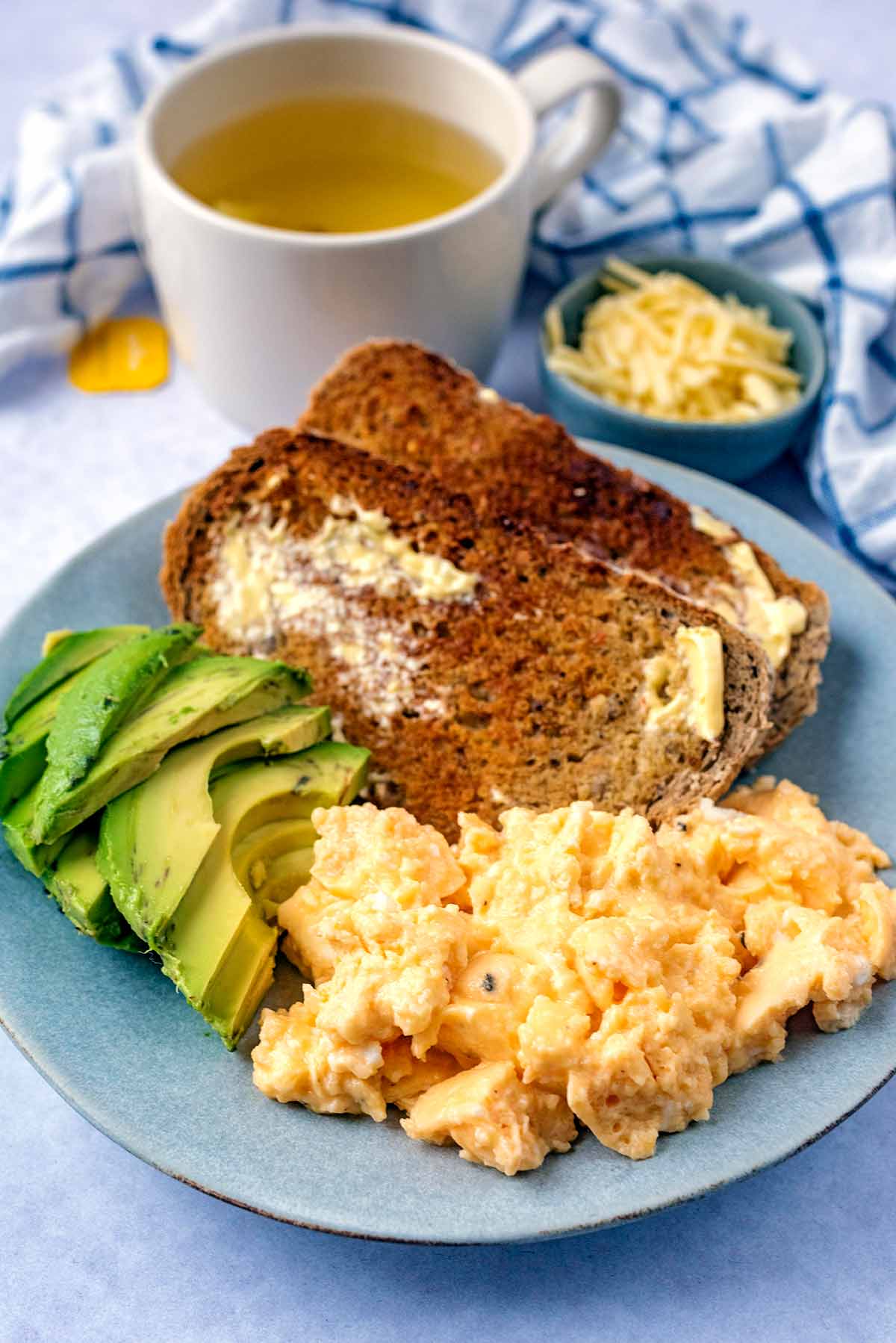Scrambled eggs and toast in front of a mug of fruit tea.
