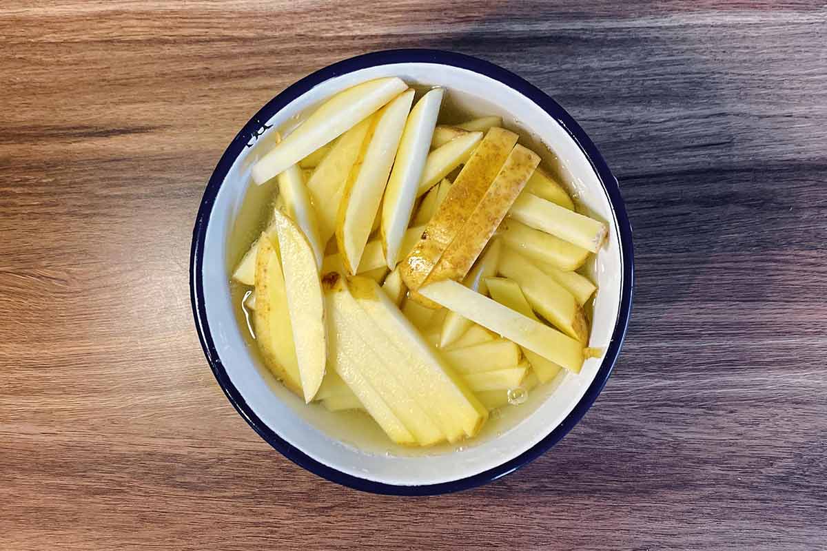 Potato cut into chips in a bowl of water.