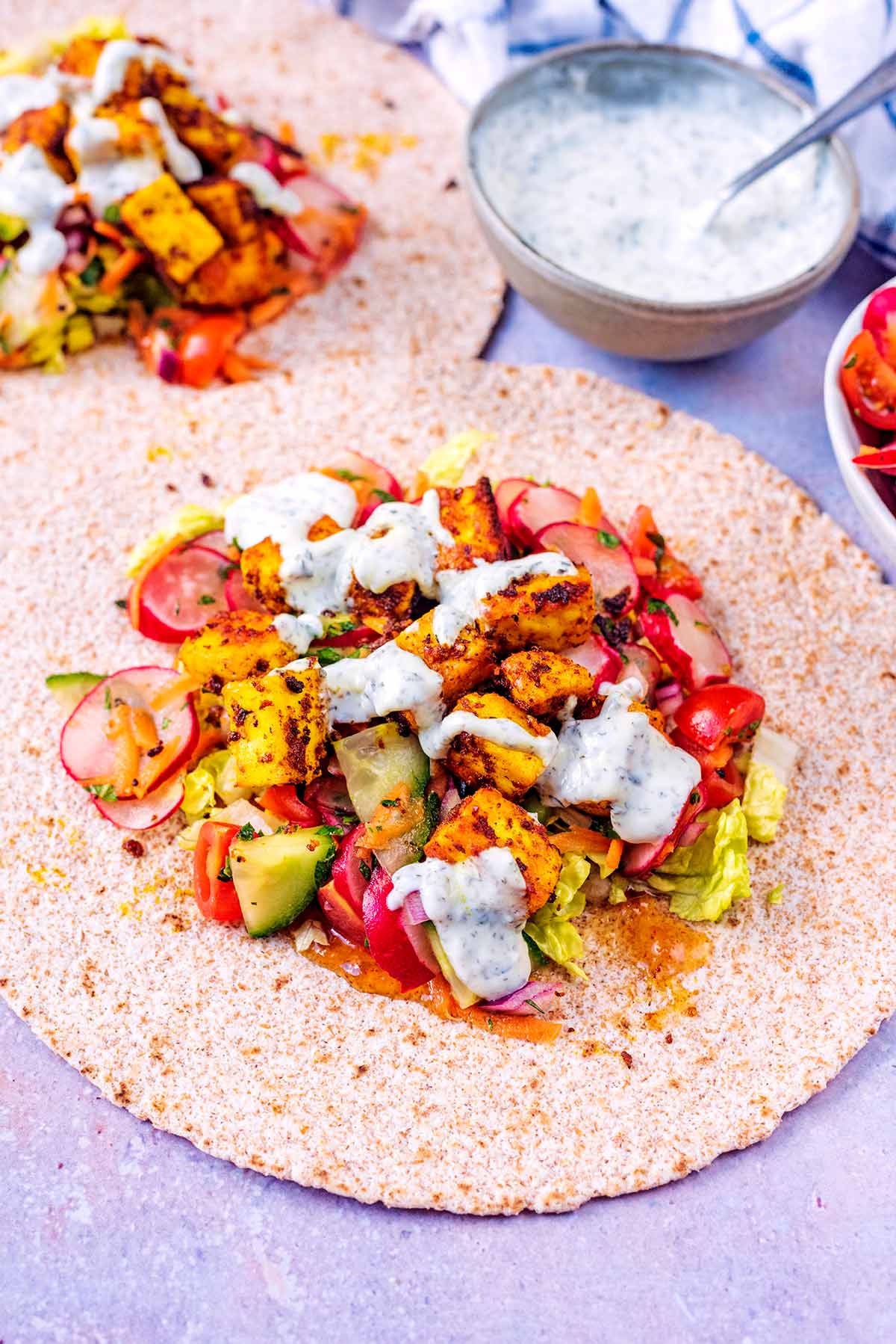 A paneer wrap in front of a bowl of mint yogurt.