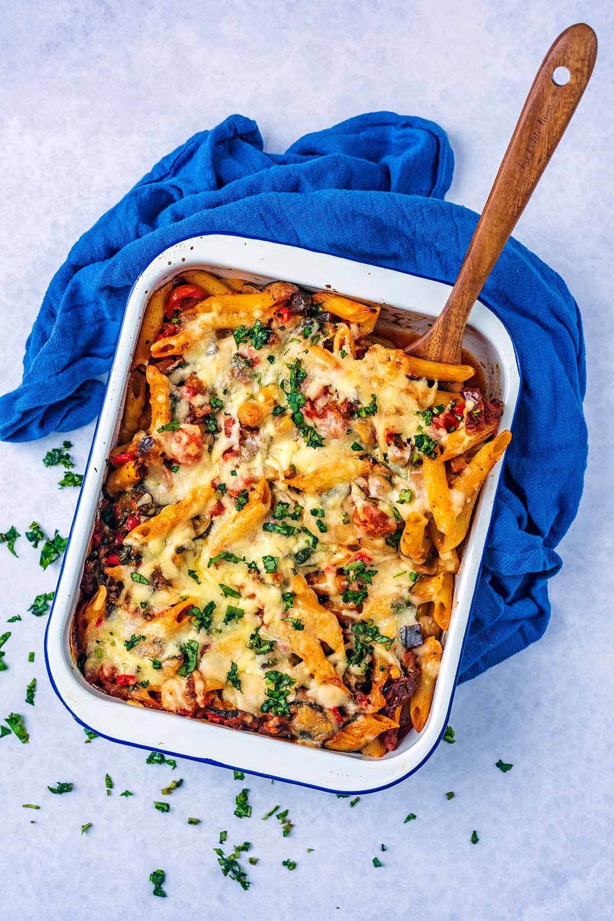 A large baking dish full of pasta bake. A wooden spoon is pushed into it.