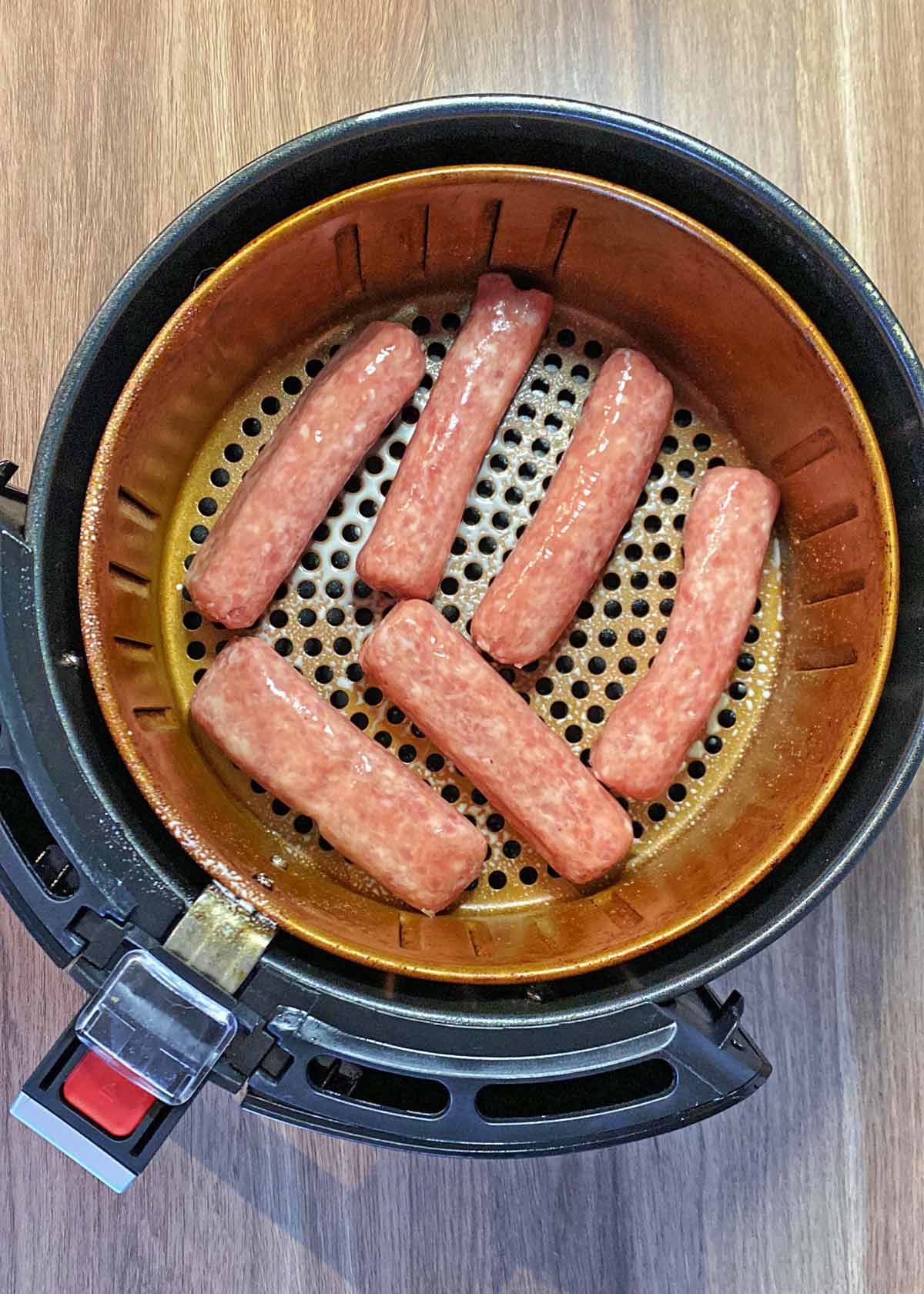 Six raw sausages in an air fryer basket.