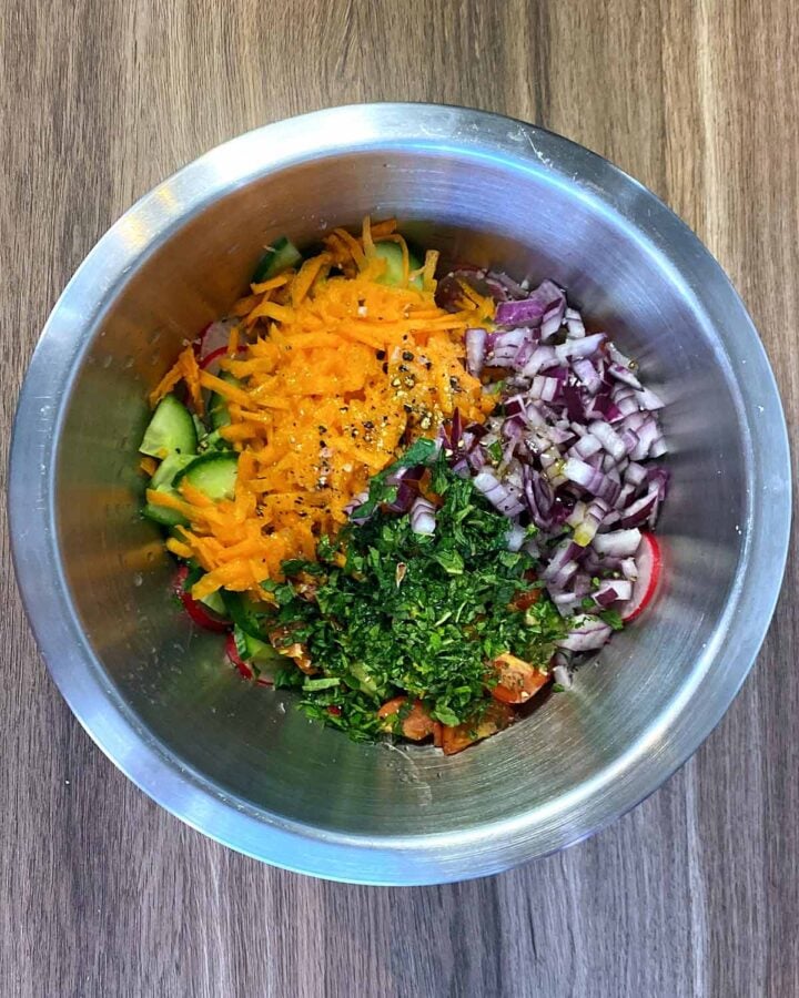 Grated carrot, diced onion, herbs and dressing added to the bowl.