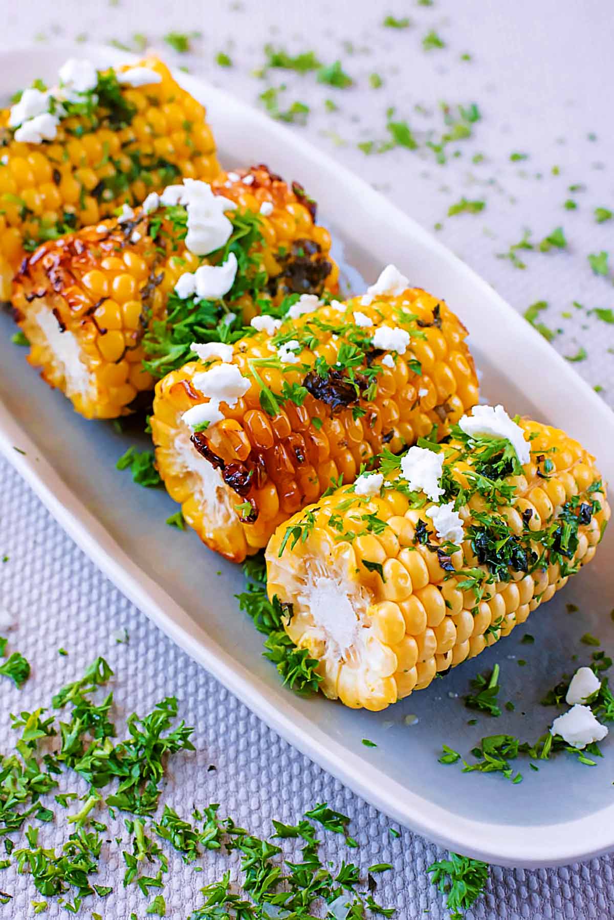 Four corn on the cob with char marks topped with herbs and feta.