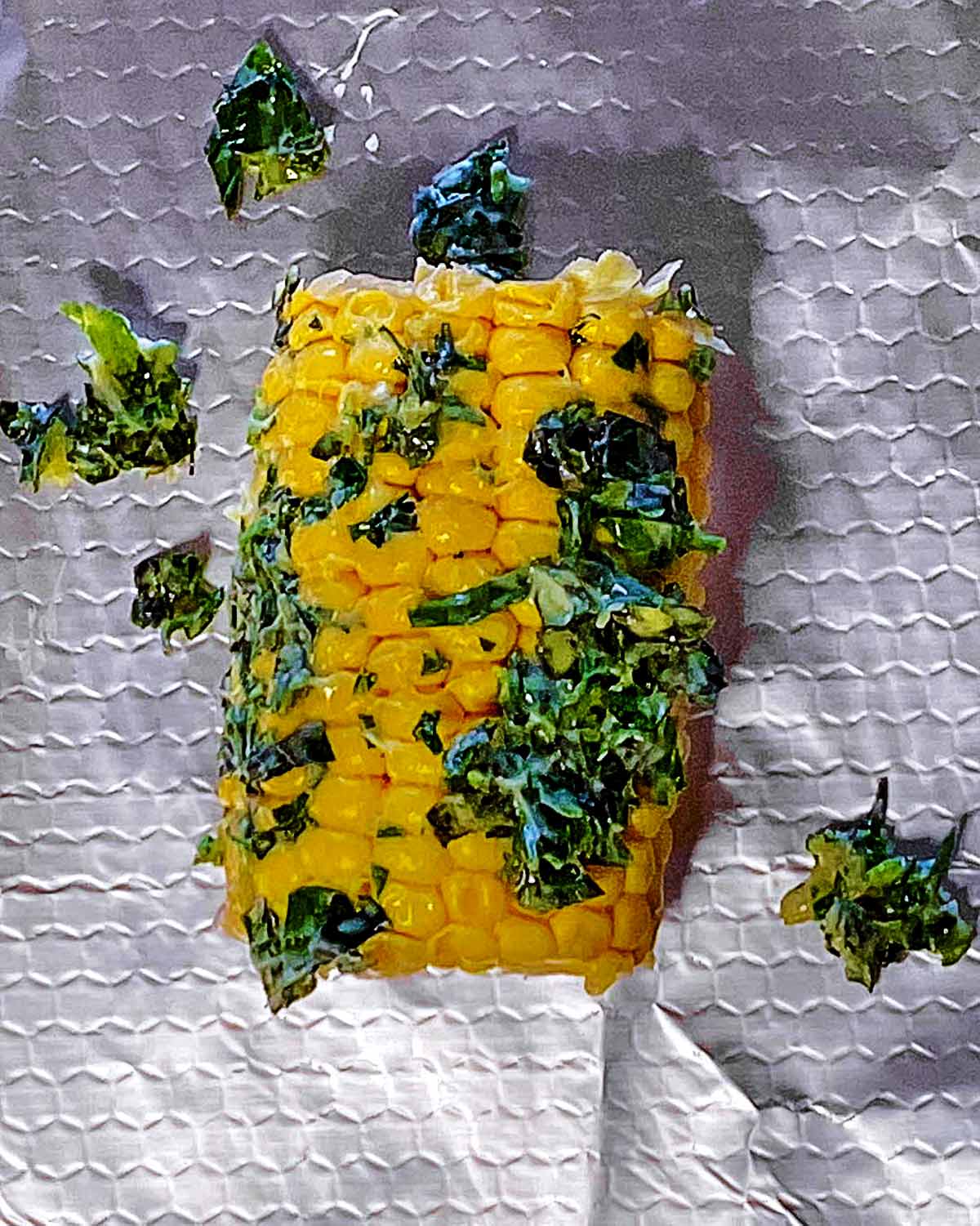 An ear of corn smothered in herb butter sat on some aluminium foil.