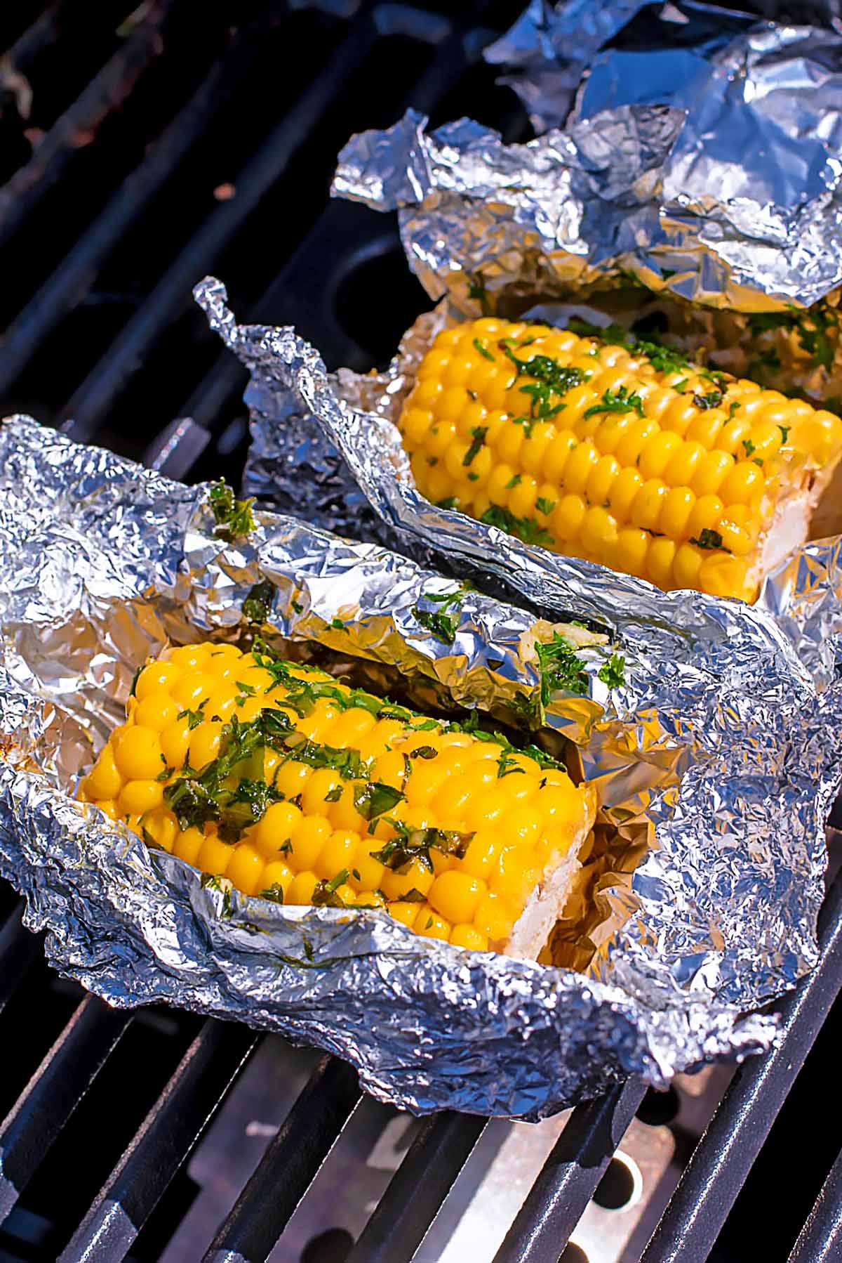 Corn wrapped in open foil on a barbecue grill.