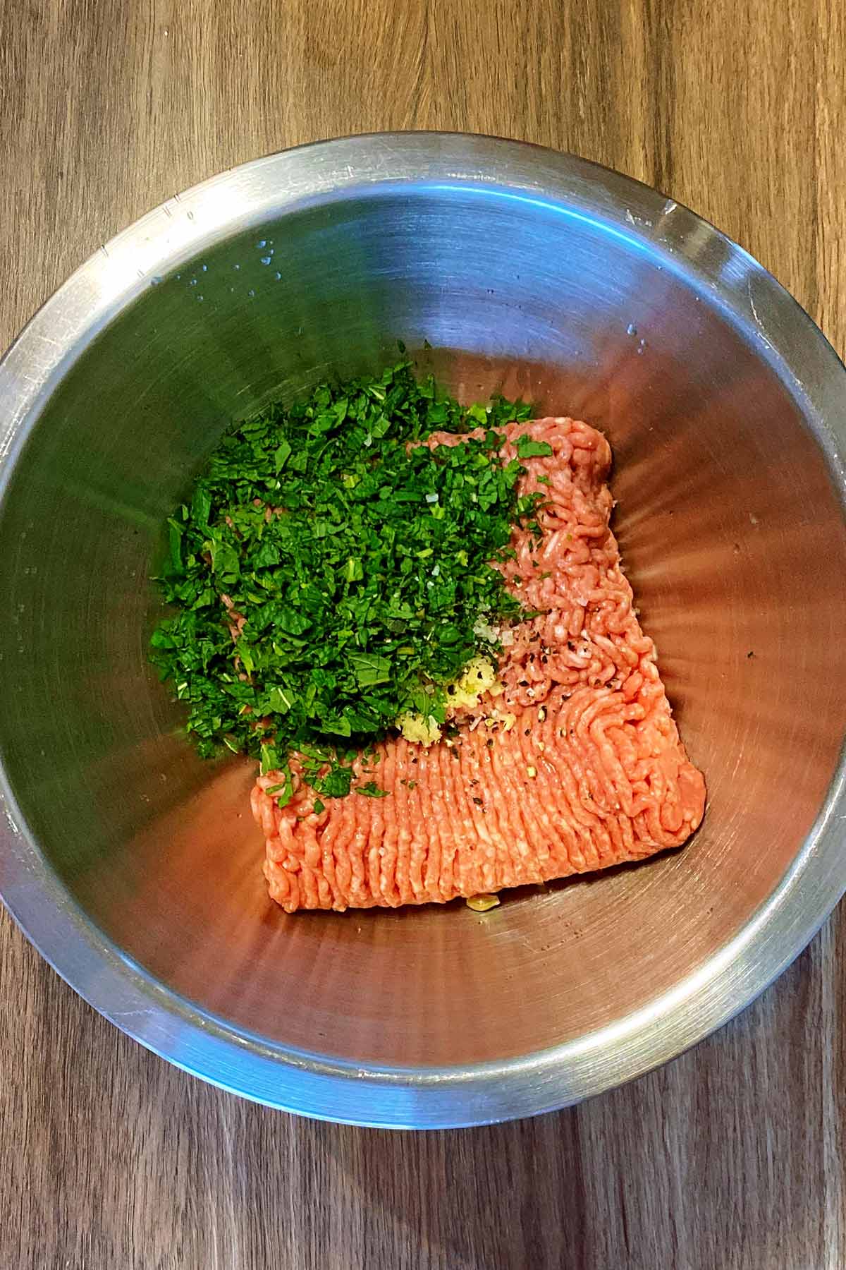 Minced lamb, chopped herbs and crushed garlic in a mixing bowl.