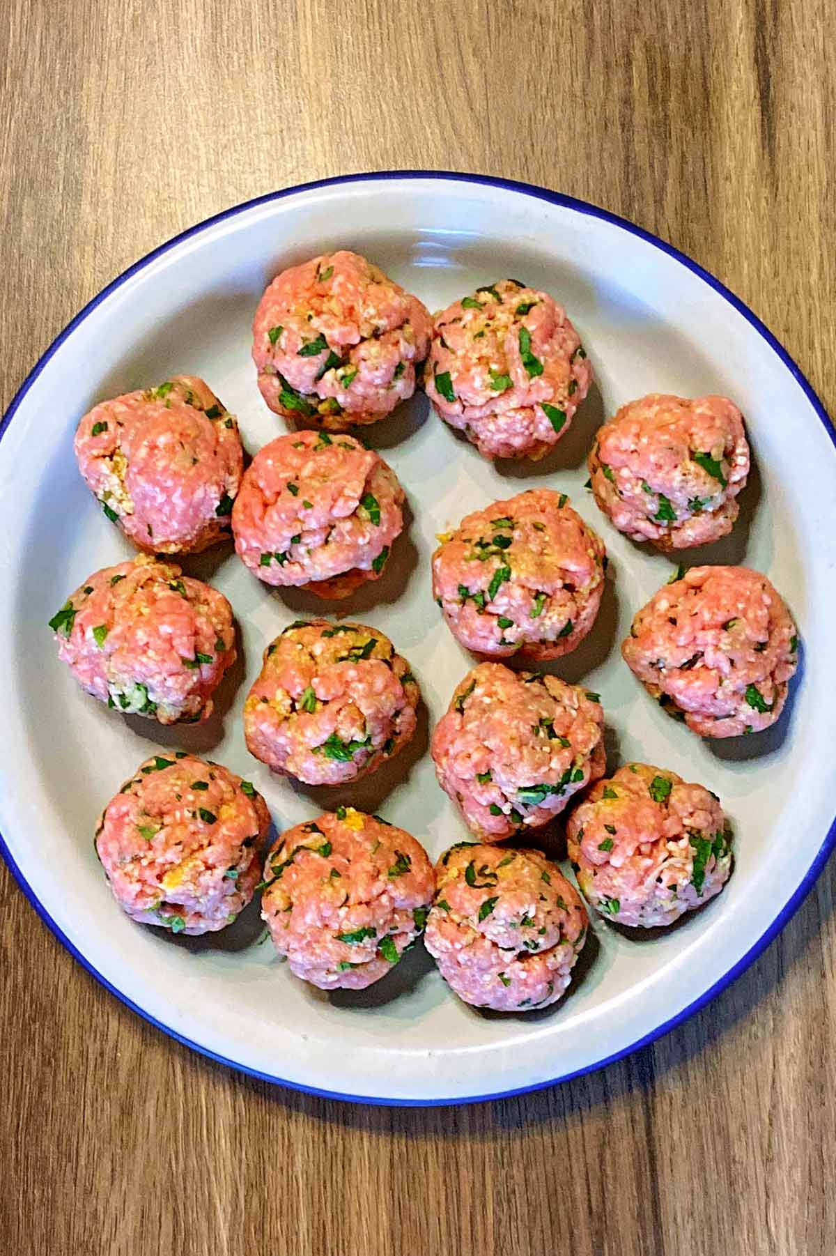 Uncooked meatballs on a round white plate.