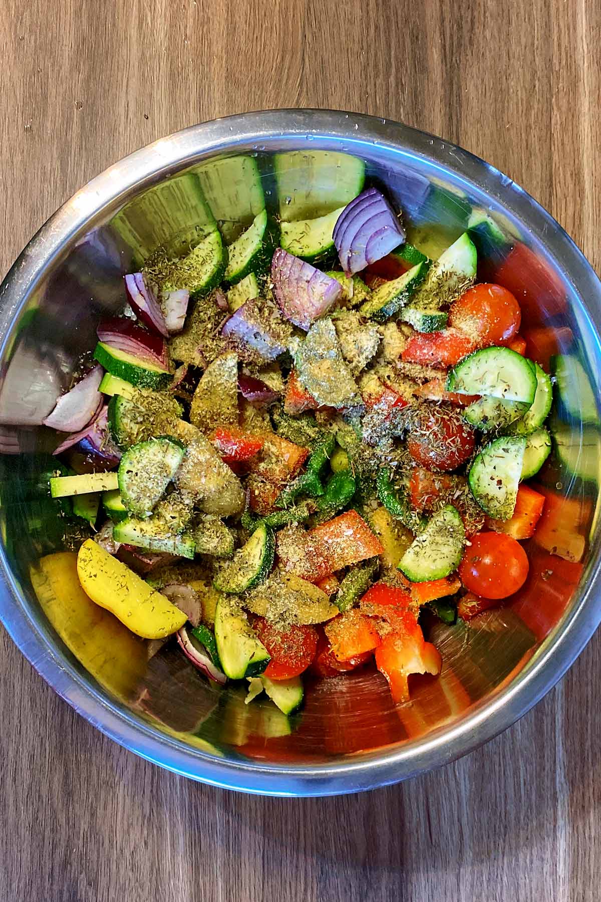 Chopped vegetables in a mixing bowl with dried herbs sprinkled over them,