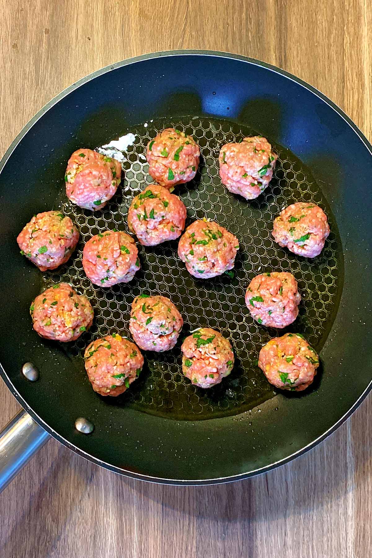 A frying pan with meatballs browning in it.