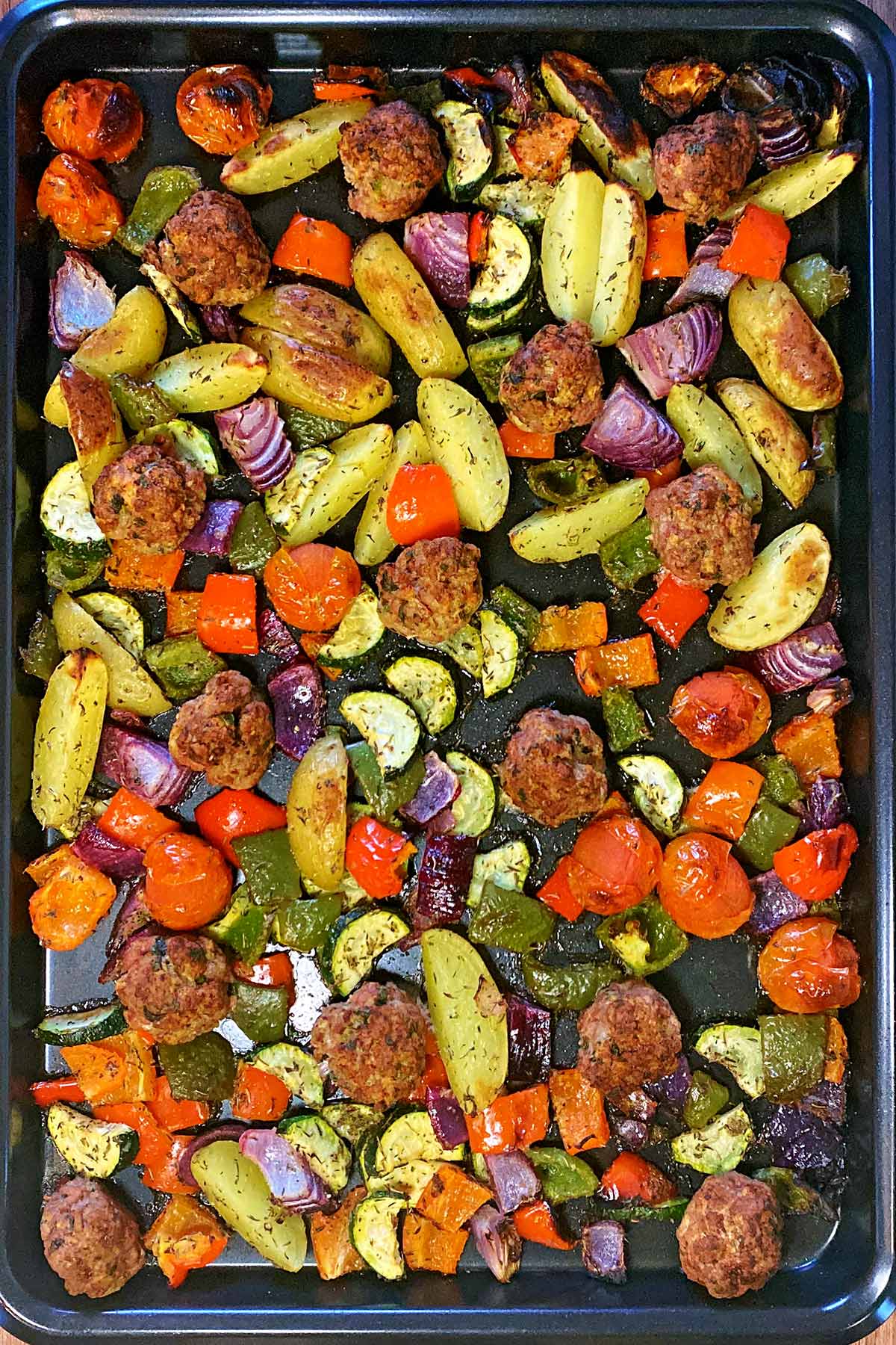 Cooked meatballs and vegetables on a baking tray.