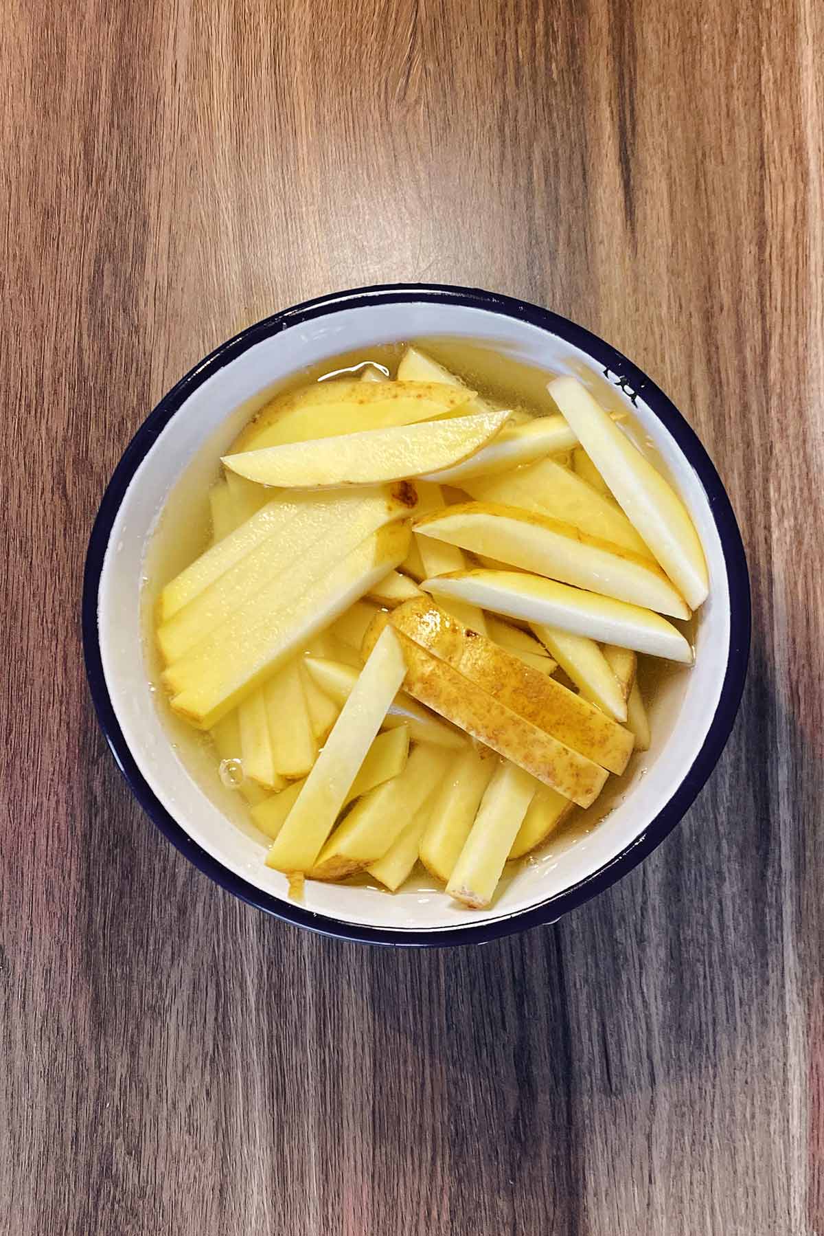 Potato cut into chips in a bowl of water.