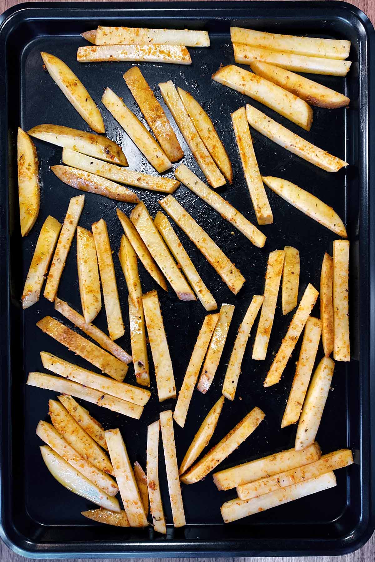 Uncooked seasoned chips on a black baking tray.