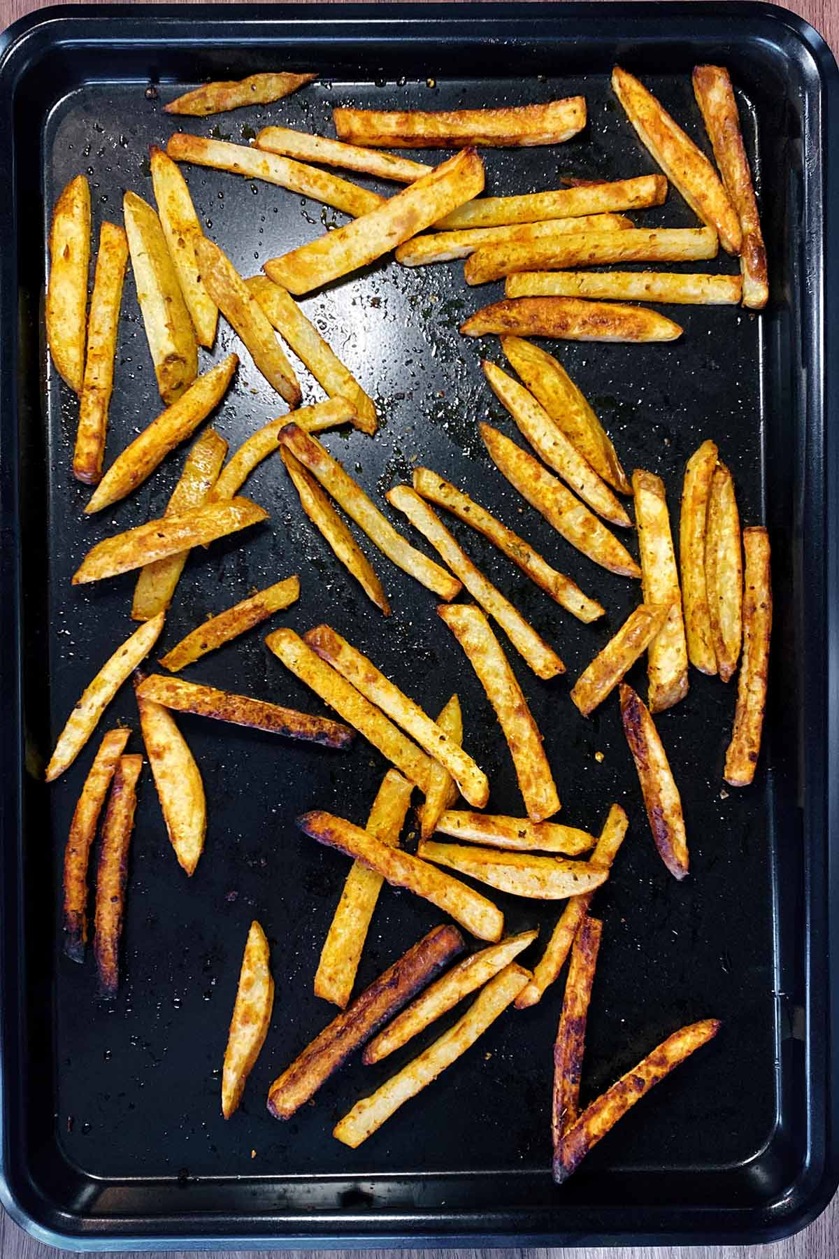 Cooked chips on a black baking tray.