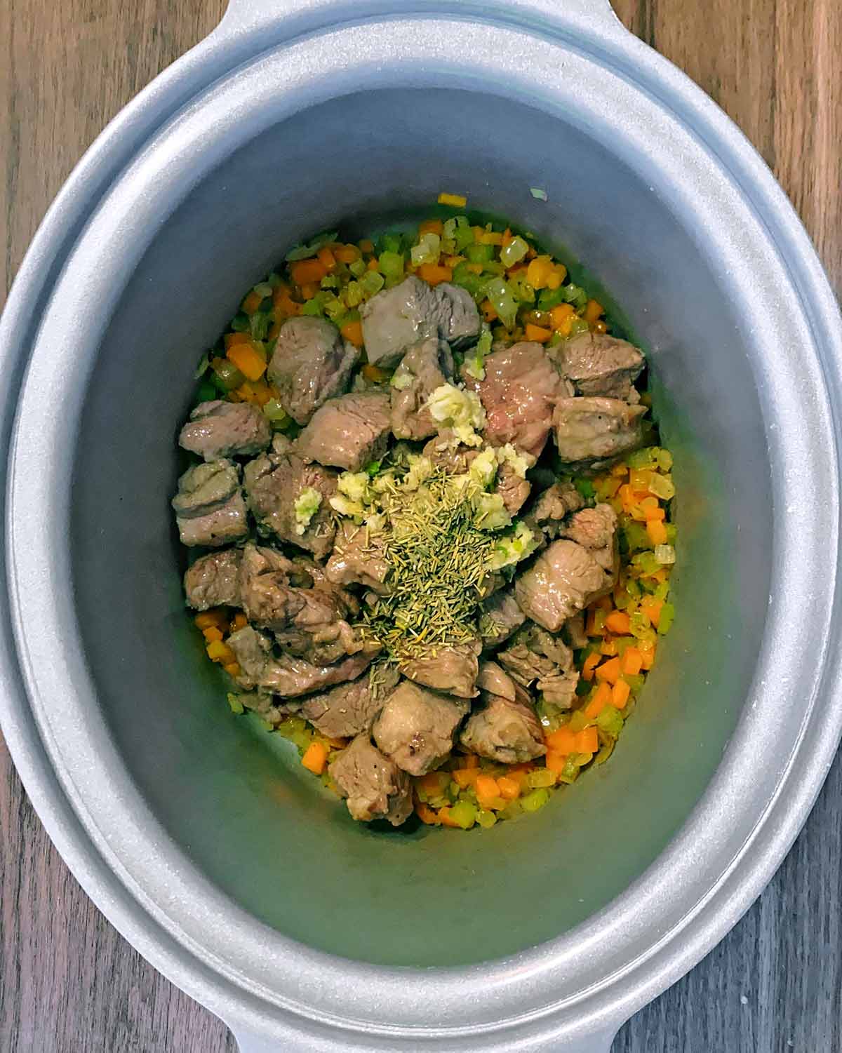 Cooked vegetables, browned lamb, crushed garlic and dried rosemary in a slow cooker pot.