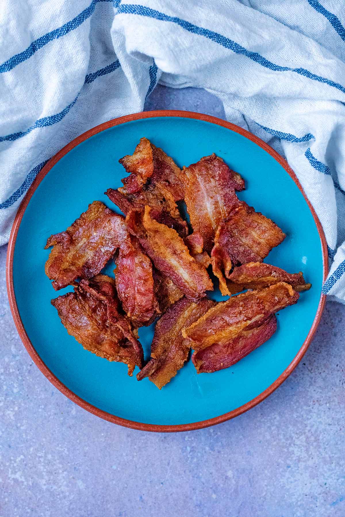 A plate of cooked bacon next to a striped towel.