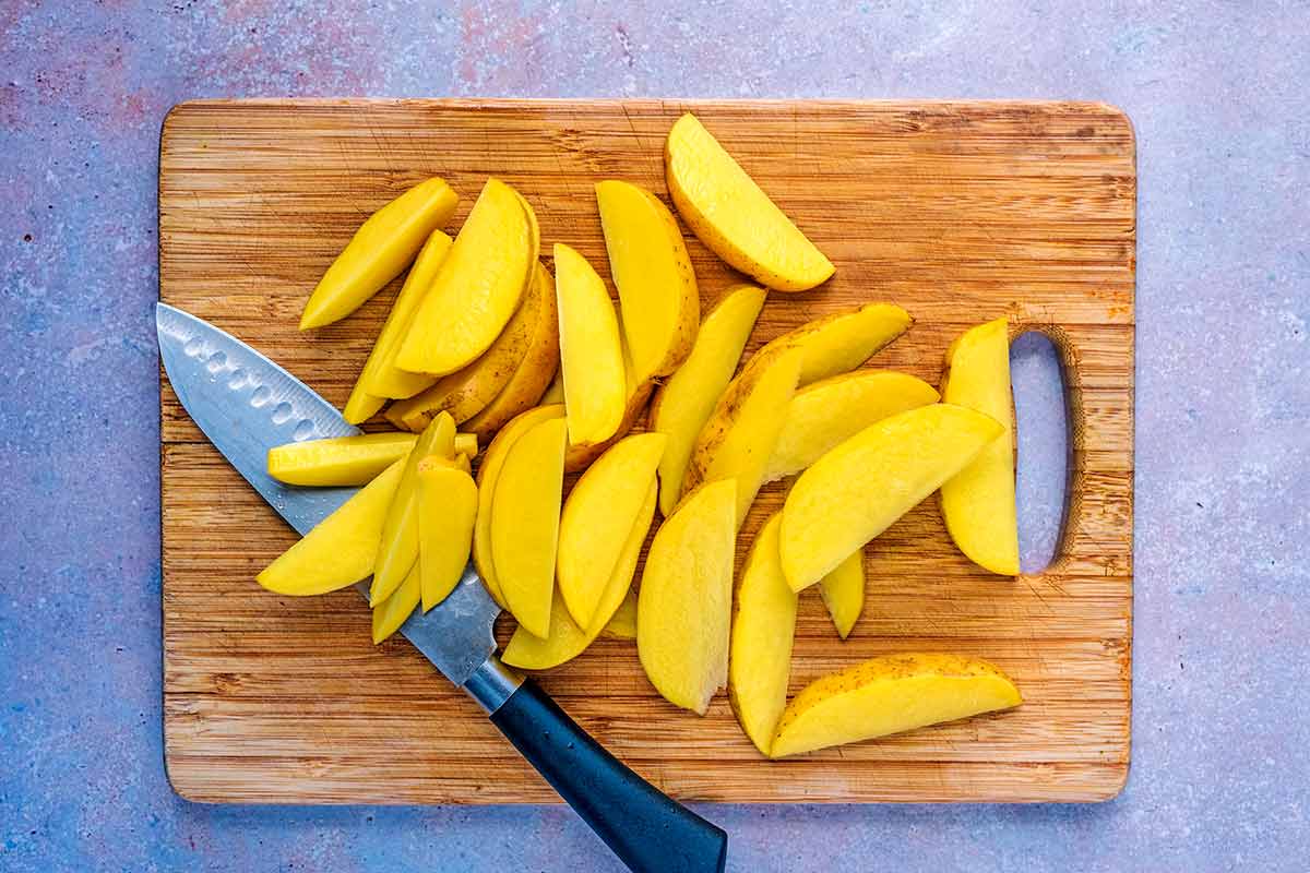 A chopping board with potatoes cut into wedges.