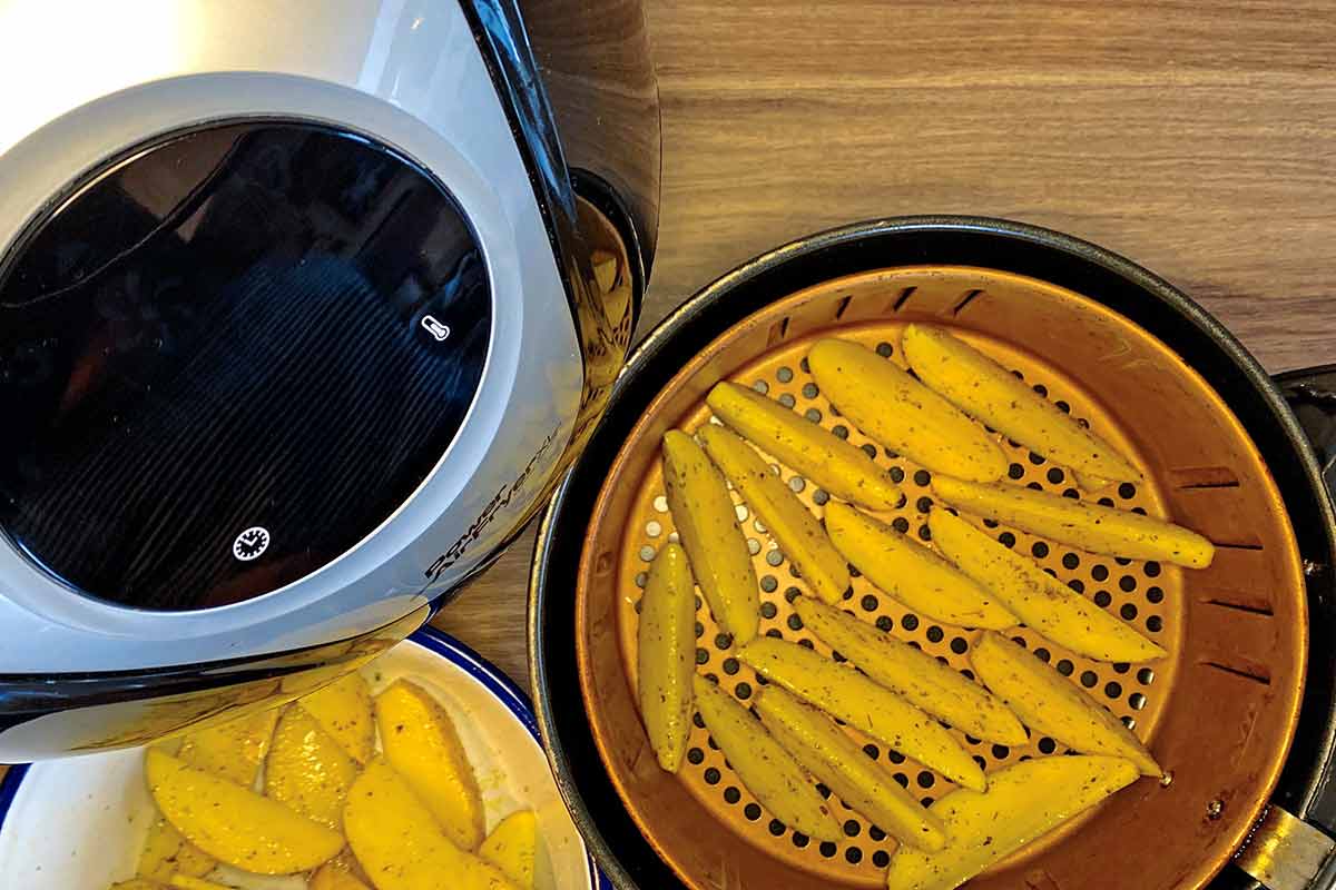 An open air fryer showing potato wedges in the basket.