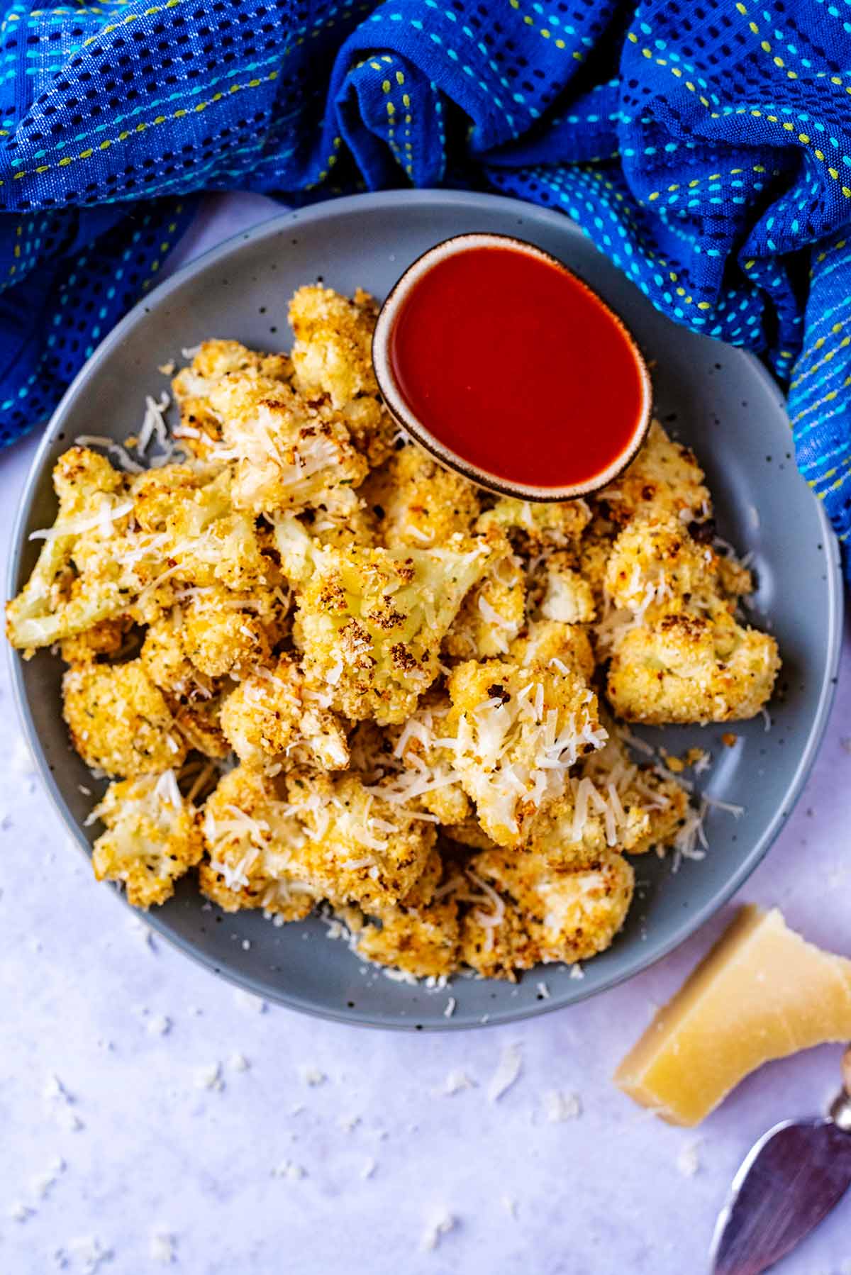 A plate of roasted crispy cauliflower florets and a small bowl of hot sauce.