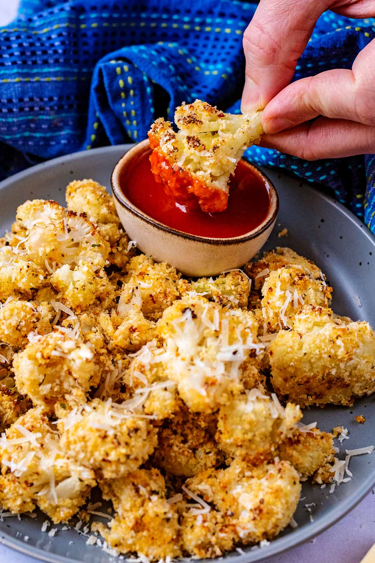A hand dipping a crispy cauliflower floret into a small bowl of sauce.