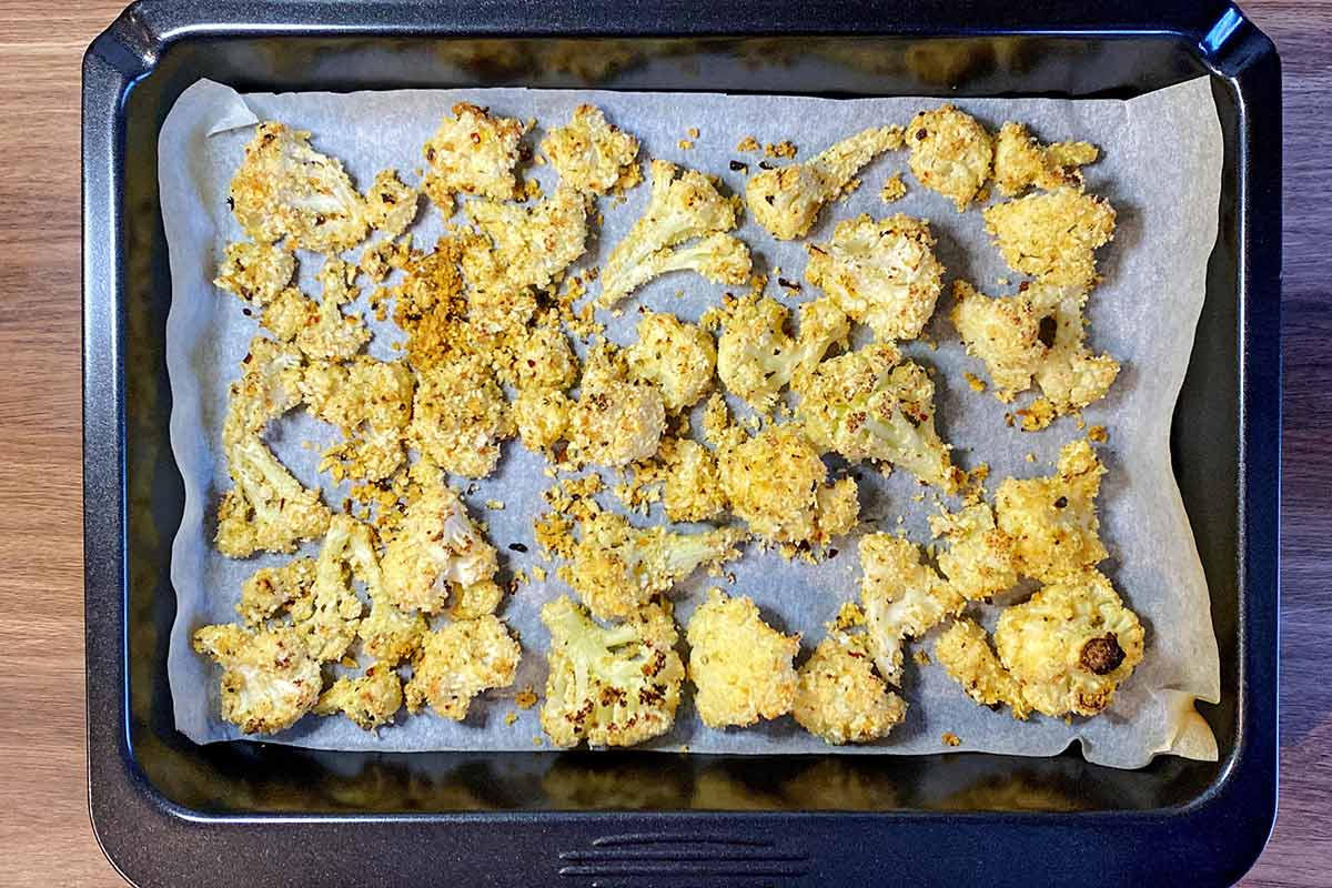 Cooked crispy cauliflower florets on a lined baking tray.