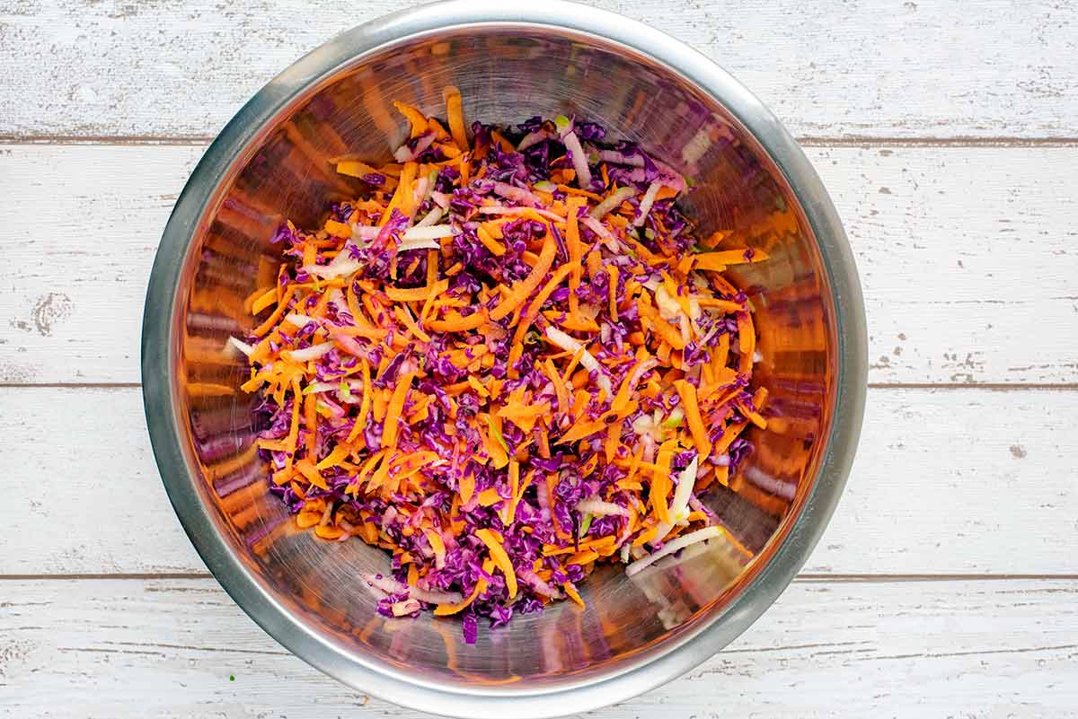 A large bowl containing grated carrot, red cabbage and apple.