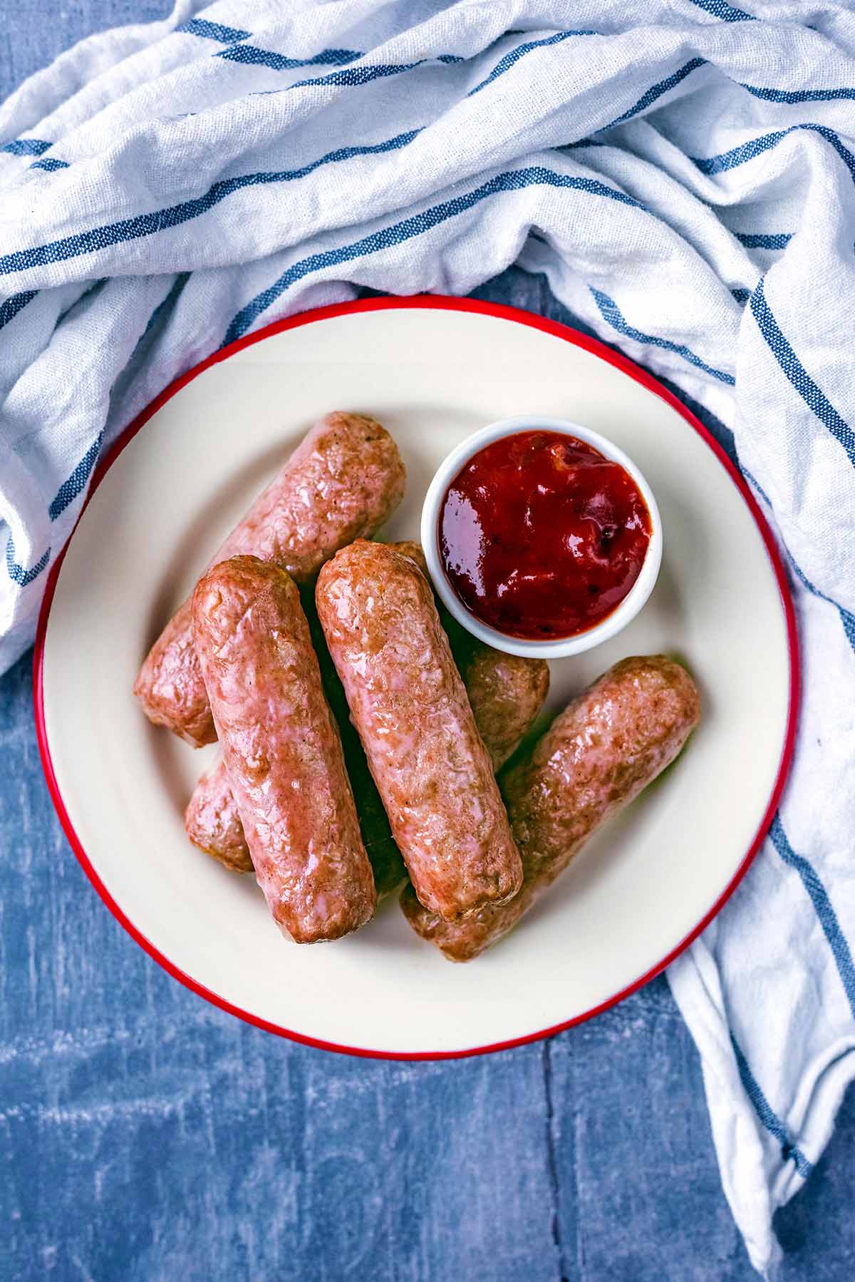 A plate of cooked sausages with a small pot of ketchup.