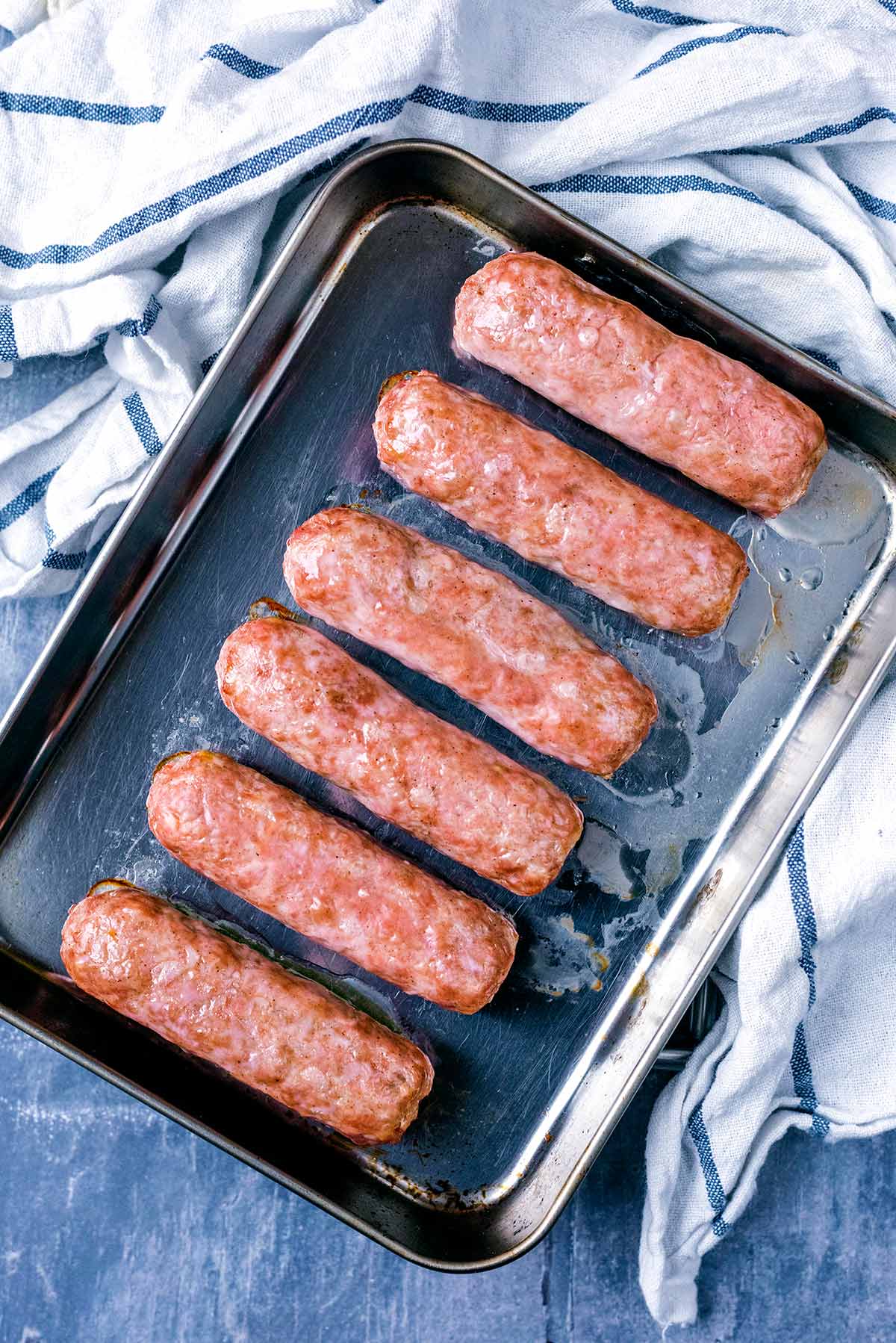 Six cooked sausages on a baking tray.