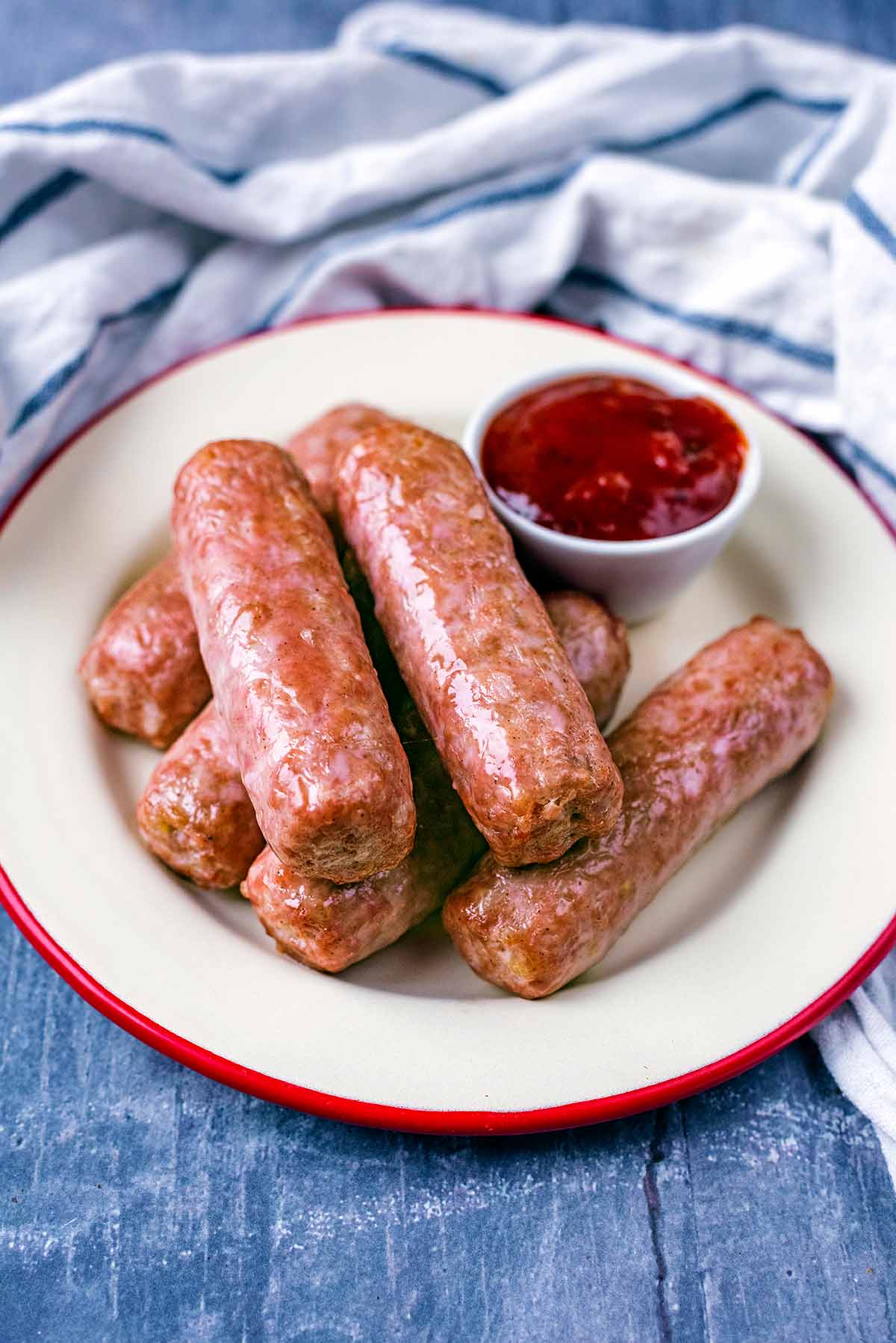 Six sausages on a plate in front of a striped towel.