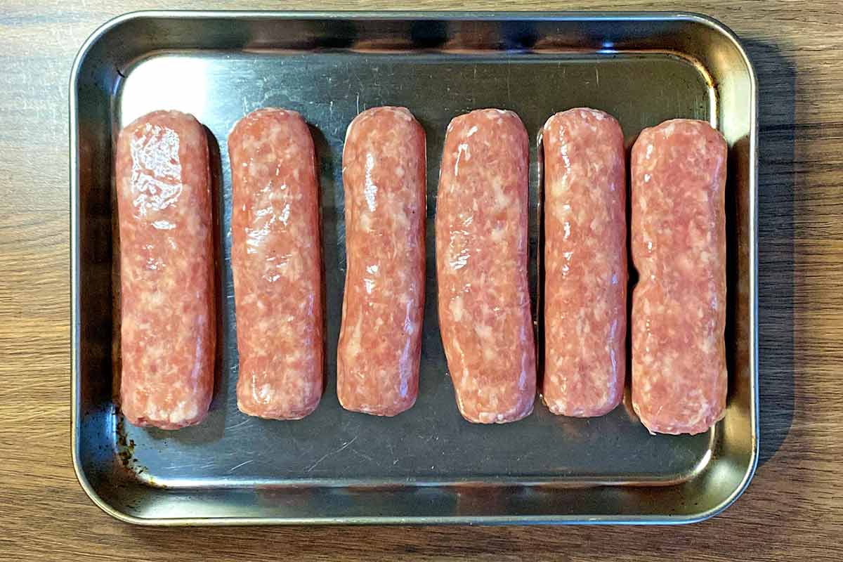 Six uncooked sausages on a baking tray.