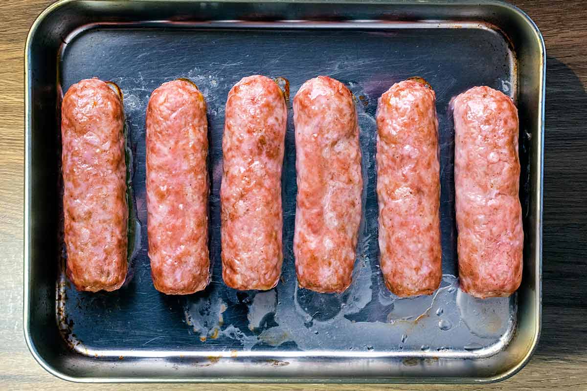 Six cooked sausages on a baking tray.