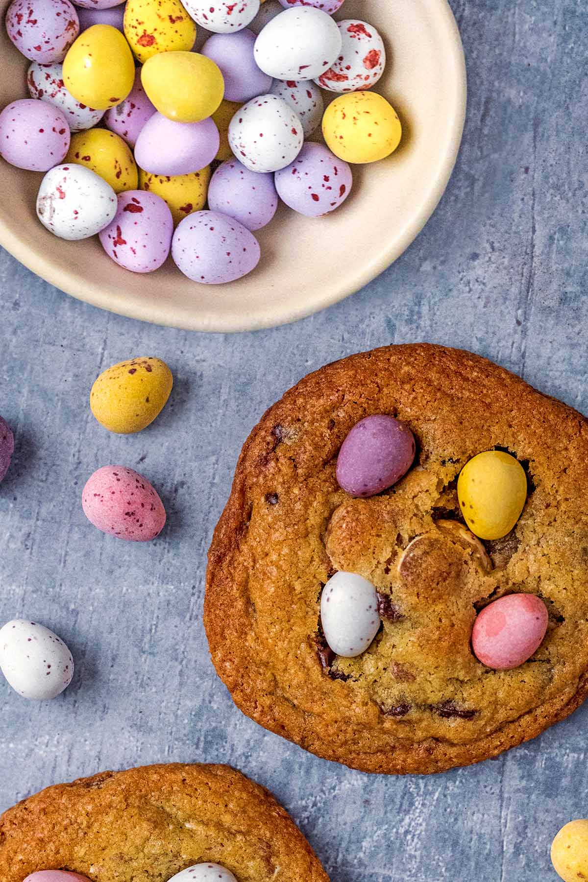 A bowl of mini eggs next to a mini egg topped cookie.
