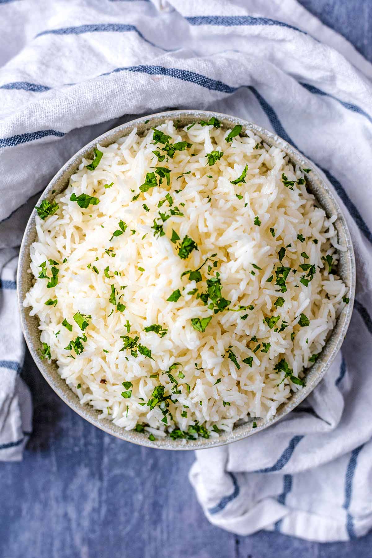A bowl of cooked white rice with chopped herbs sprinkled over it.