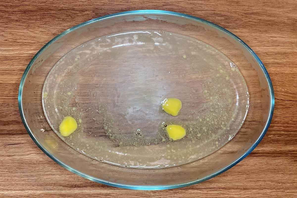 An oval glass baking dish containing water and melted butter.