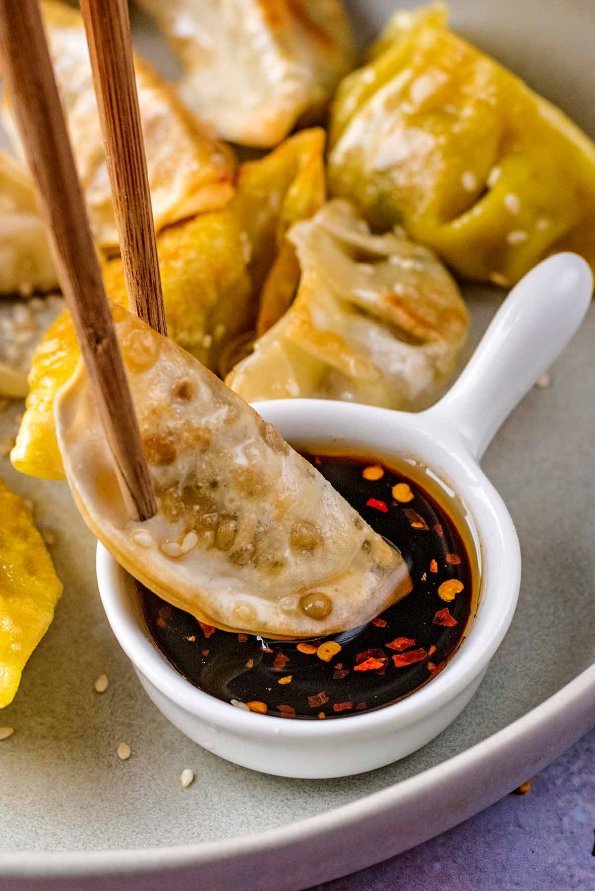 A fried gyoza being dipped into a small dish of sauce.