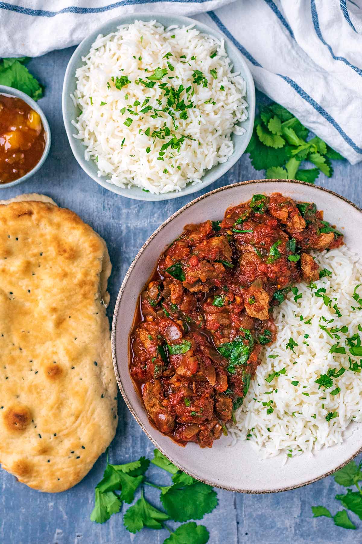 A bowl of beef curry and rice next to more rice and a naan bread.