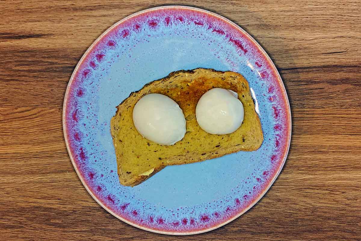 Two boiled eggs out of their shells sat on a slice of buttered toast.