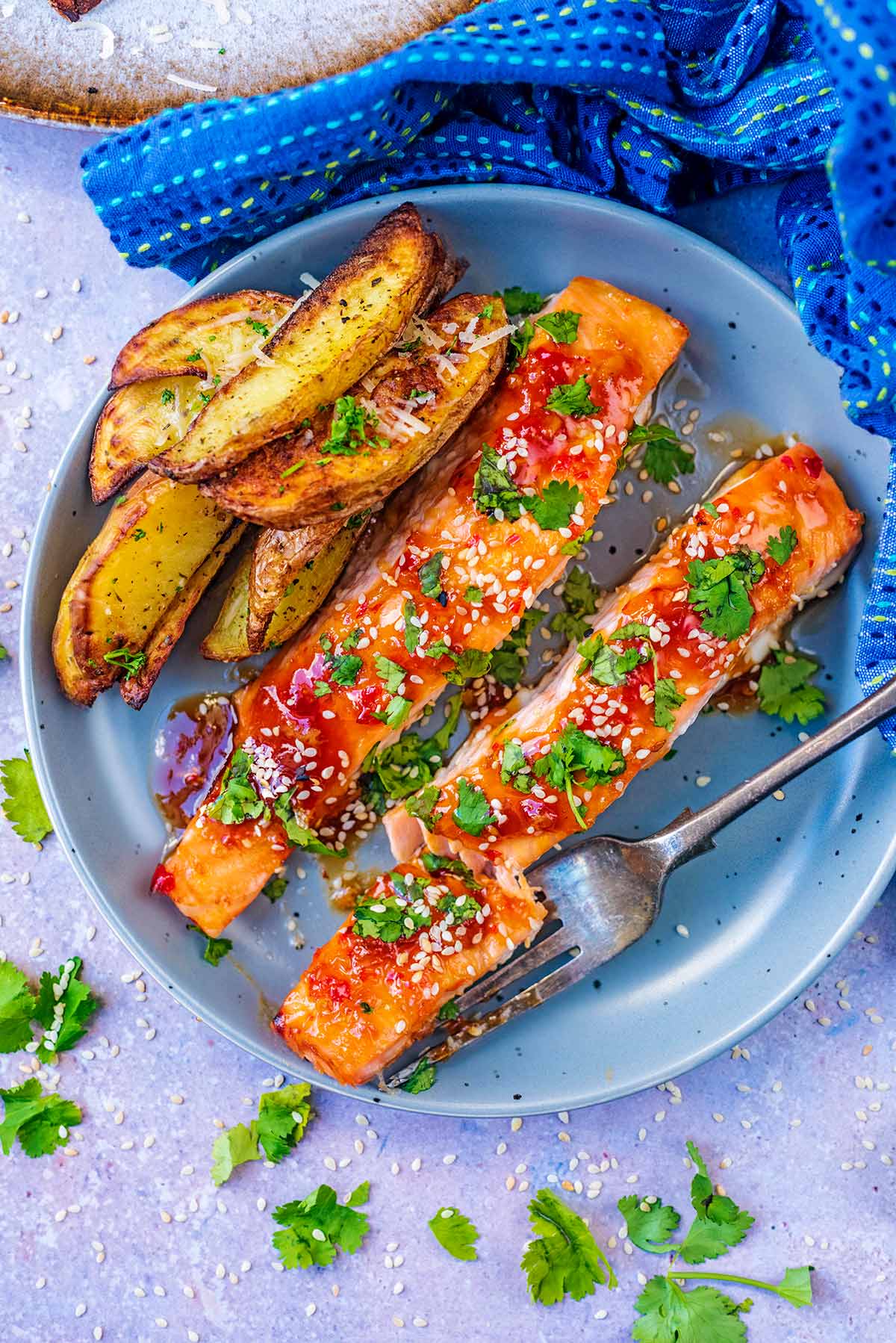 Two cooked salmon fillets and potato wedges on a round plate.