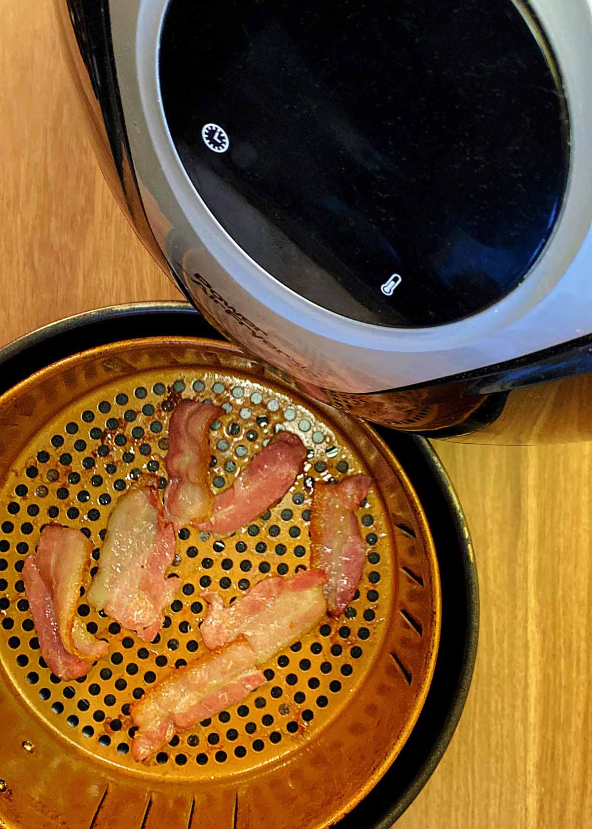 Part cooked bacon in an air fryer basket.