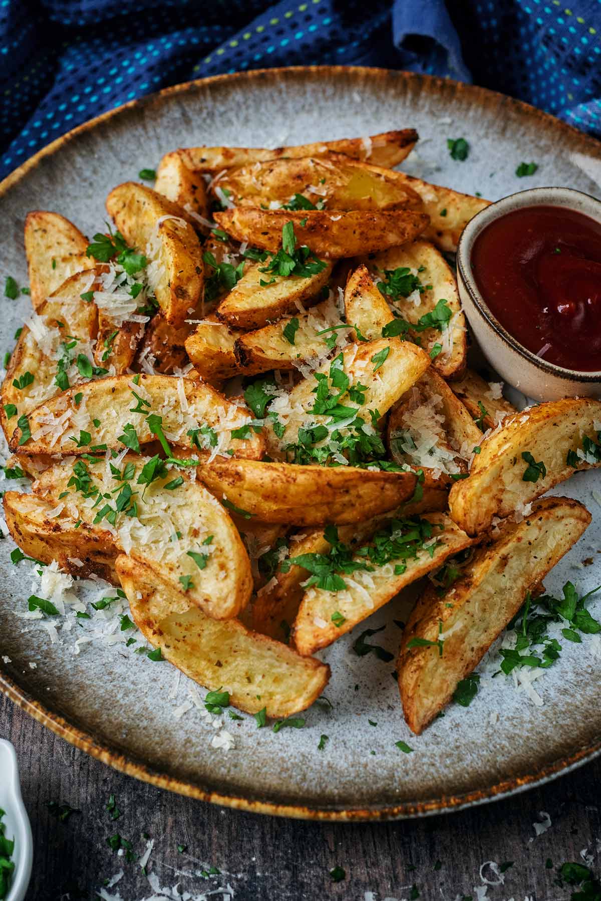 Potato wedges and ketchup on a plate in front of a blue towel.