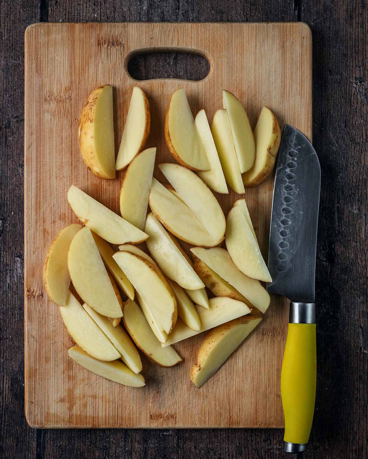 A chopping board with potatoes cut into wedges.