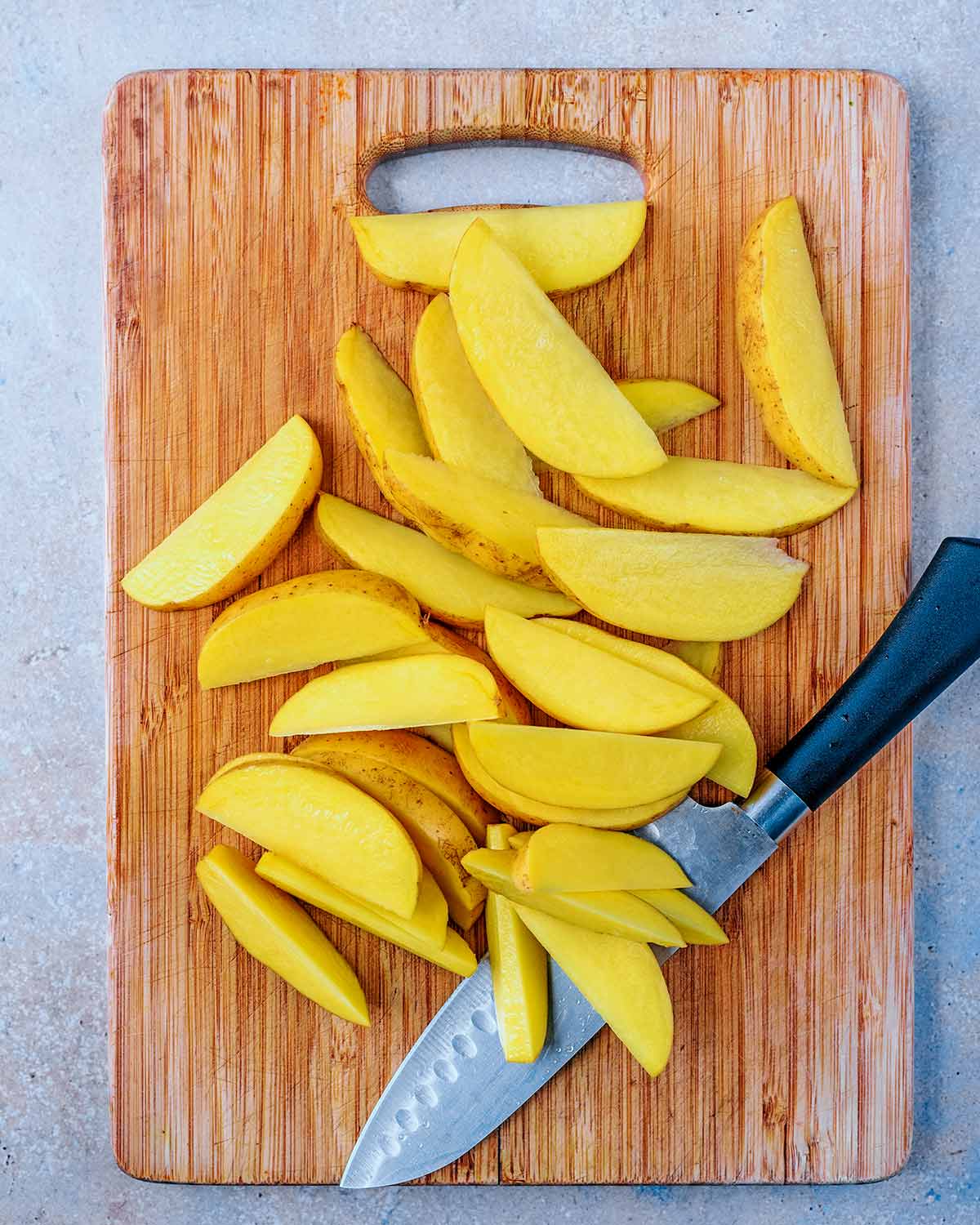 A chopping board with potatoes cut into wedges.