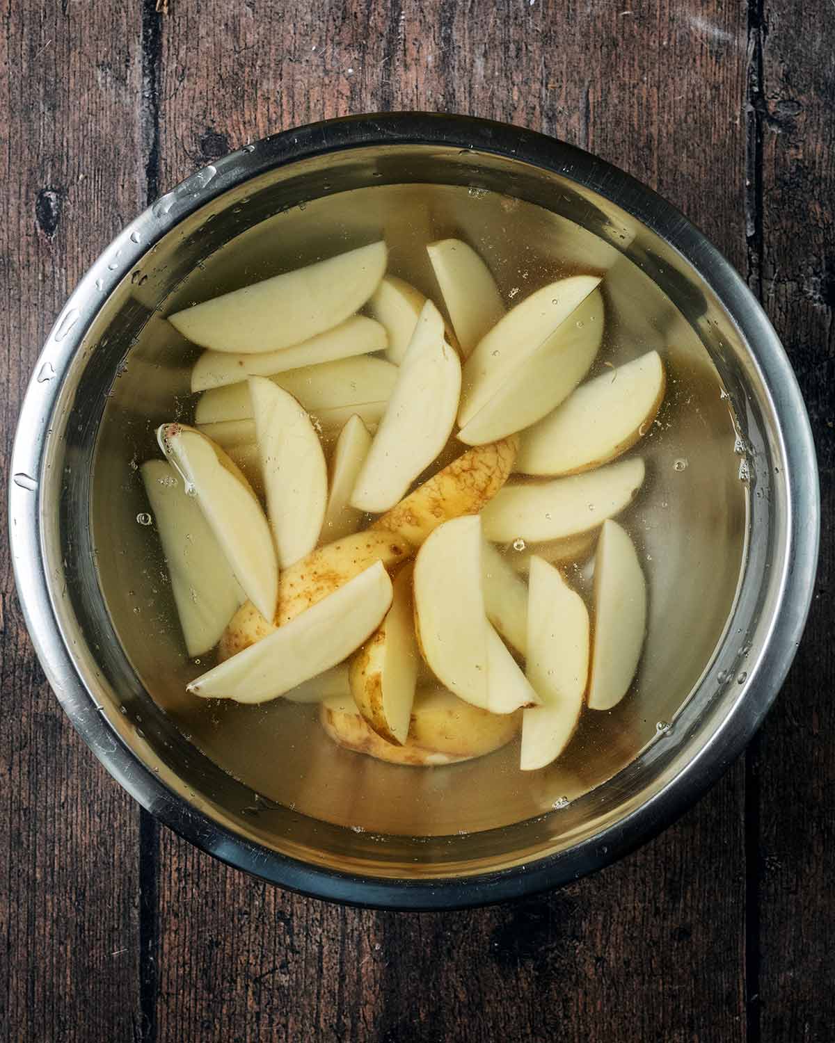 Uncooked potato wedges soaking in a bowl of water.