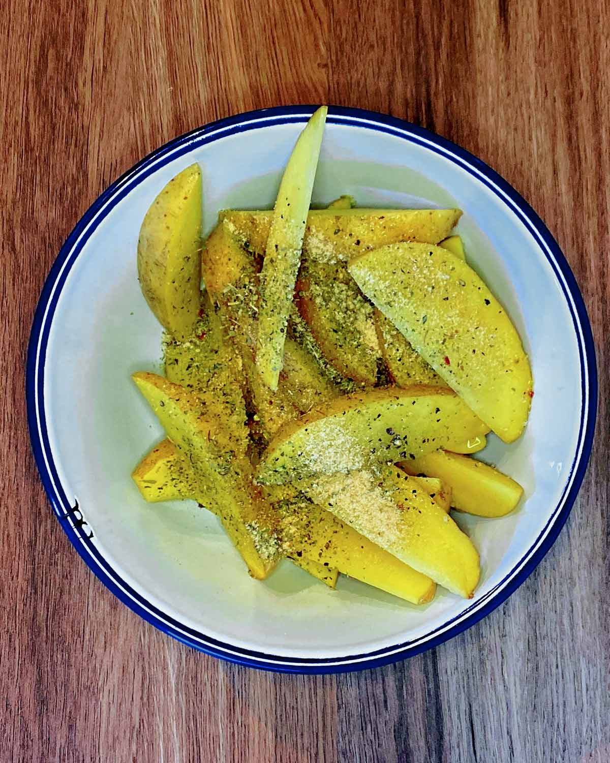 Potato wedges in a bowl with oil and seasoning.