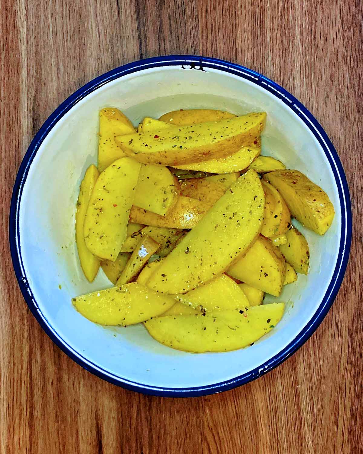 Potato wedges in a bowl coated in oil and seasoning.