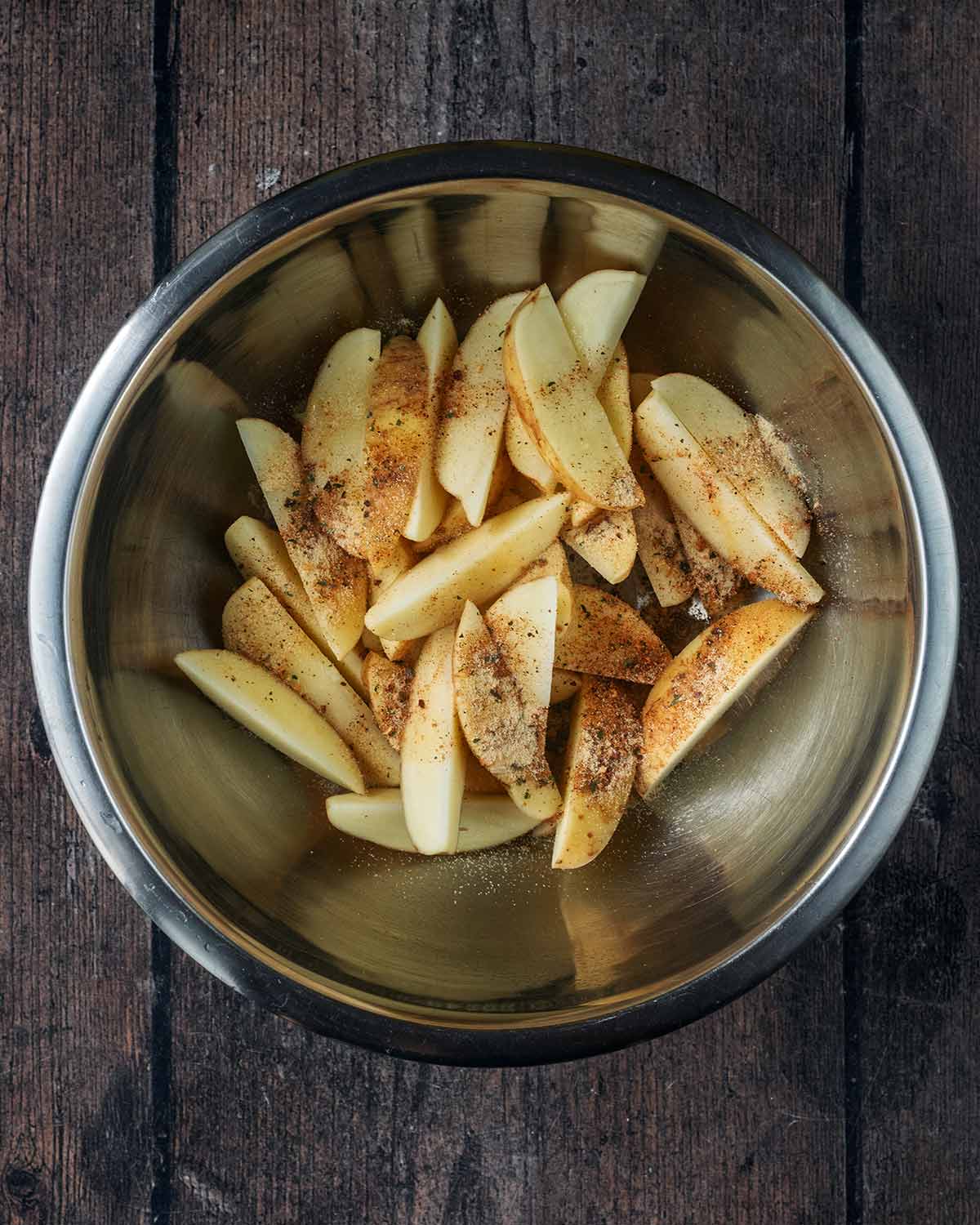 Potato wedges in a bowl with oil and seasoning.