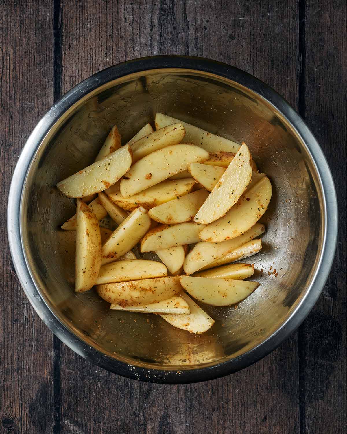 Potato wedges in a bowl coated in oil and seasoning.