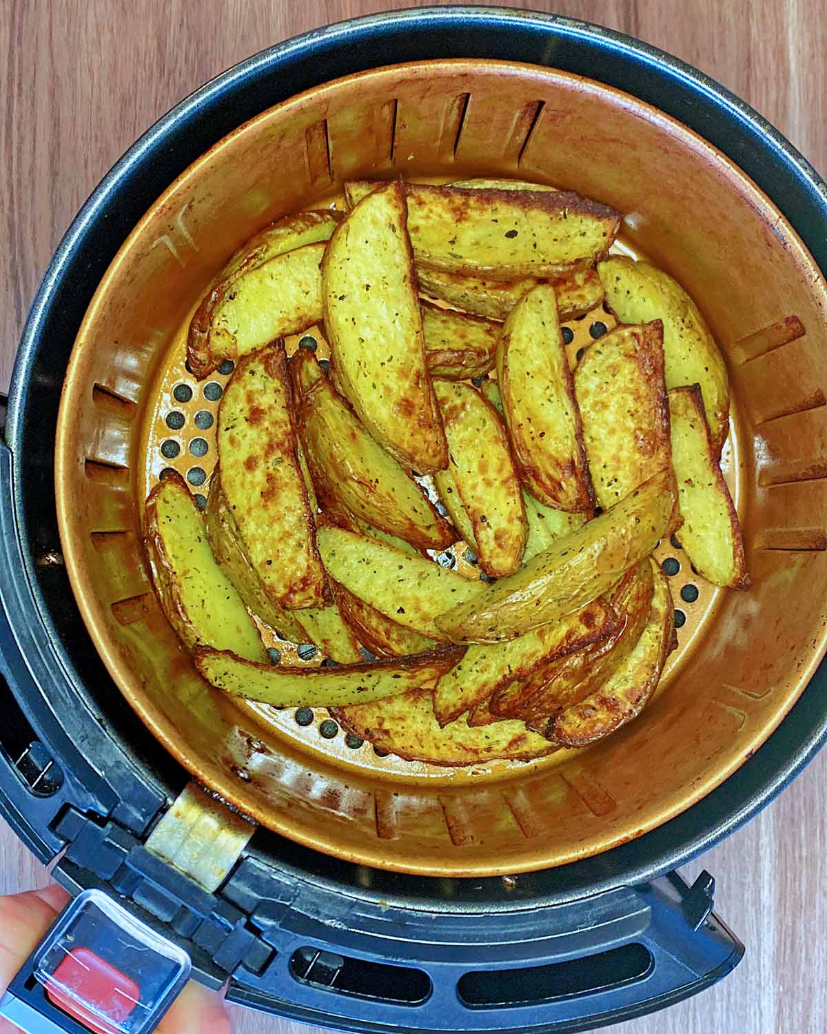 An air fryer basket containing cooked potato wedges.