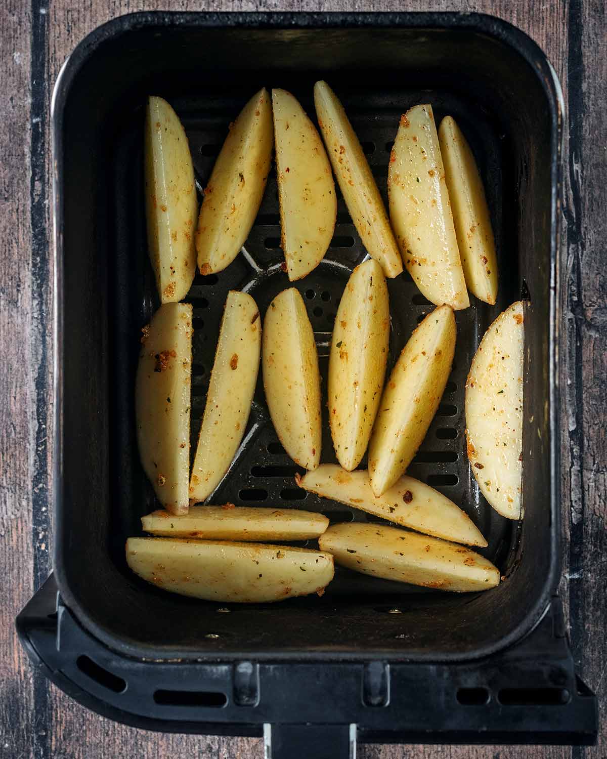 A single layer of uncooked potato wedges in an air fryer basket.