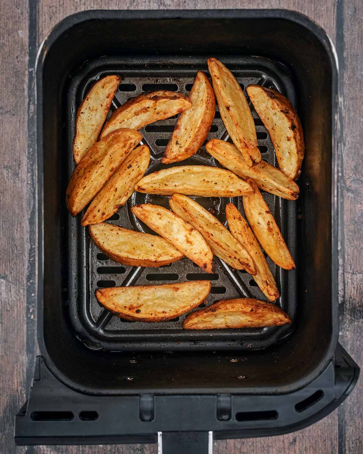 Cooked potato wedges in an air fryer basket.
