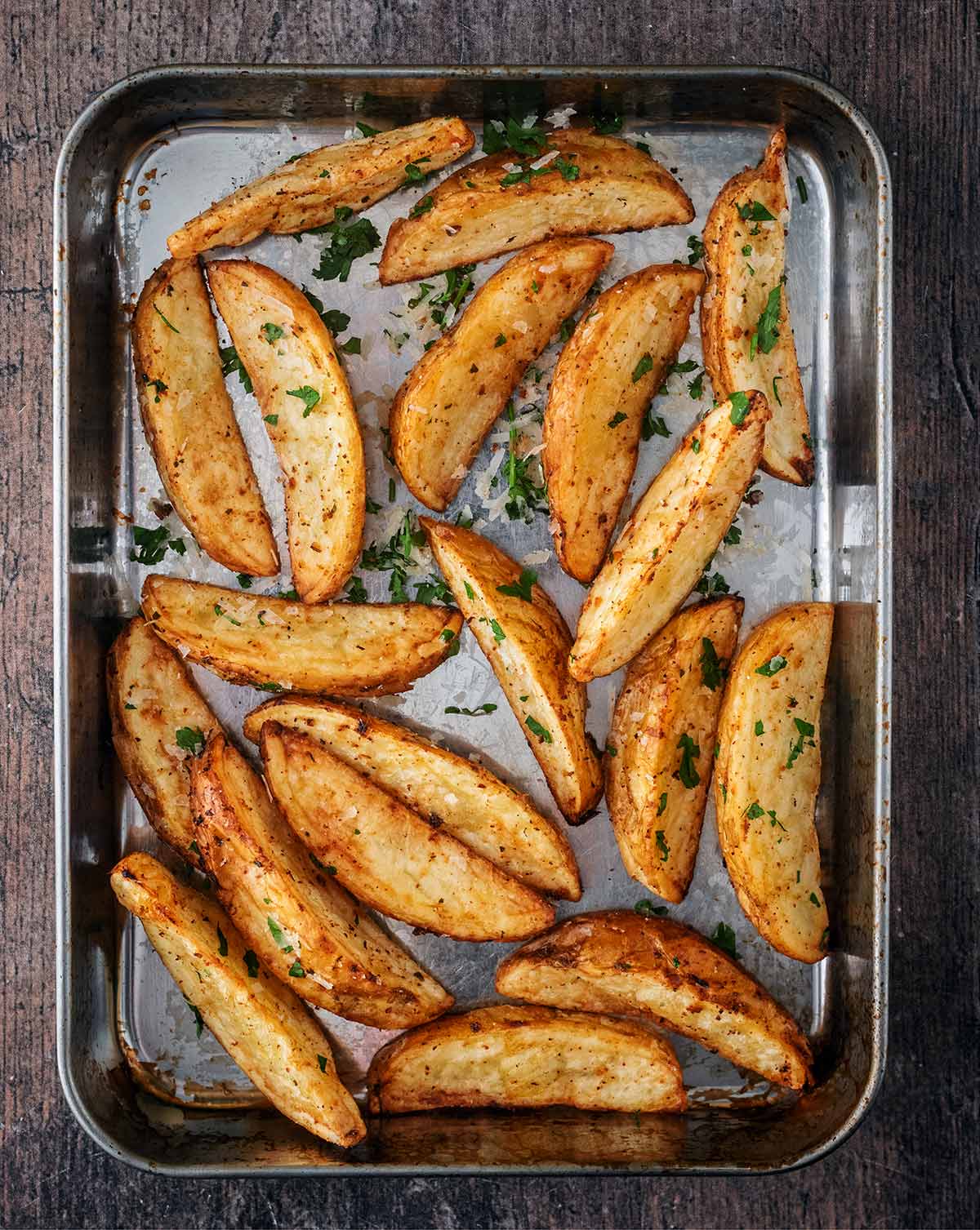 Cooked potato wedges cooling on a small baking tray.